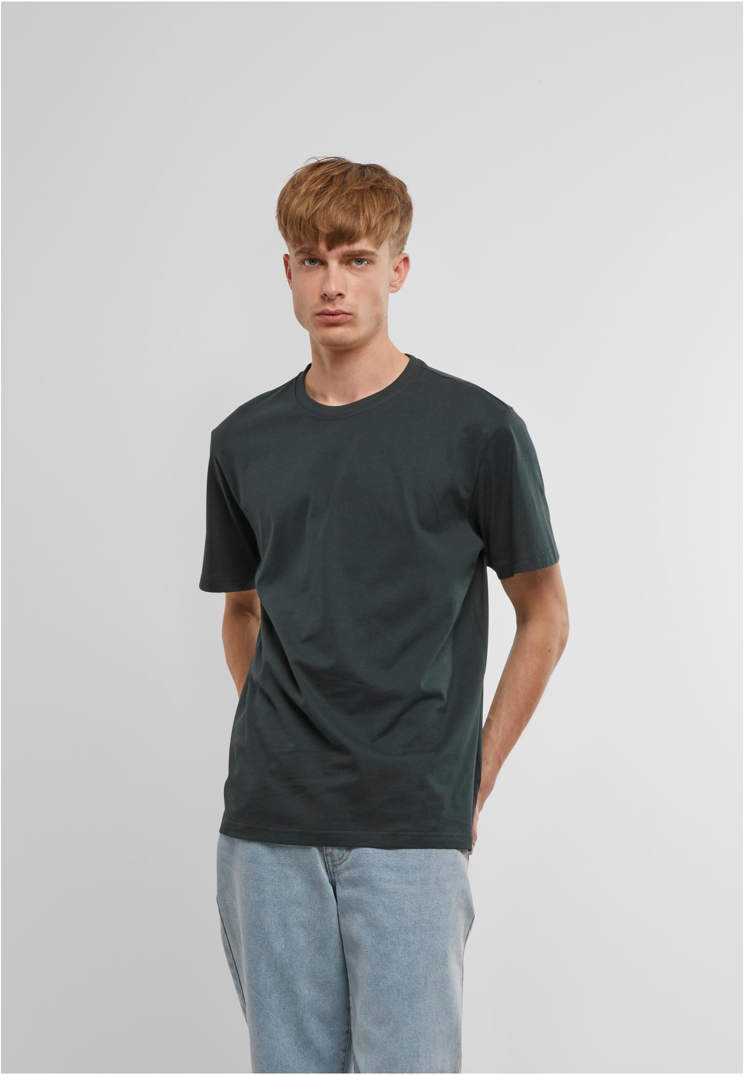 Manlig modell som bär en mörkgrön B Premium Shirt och ljusblå jeans framför en vit bakgrund.