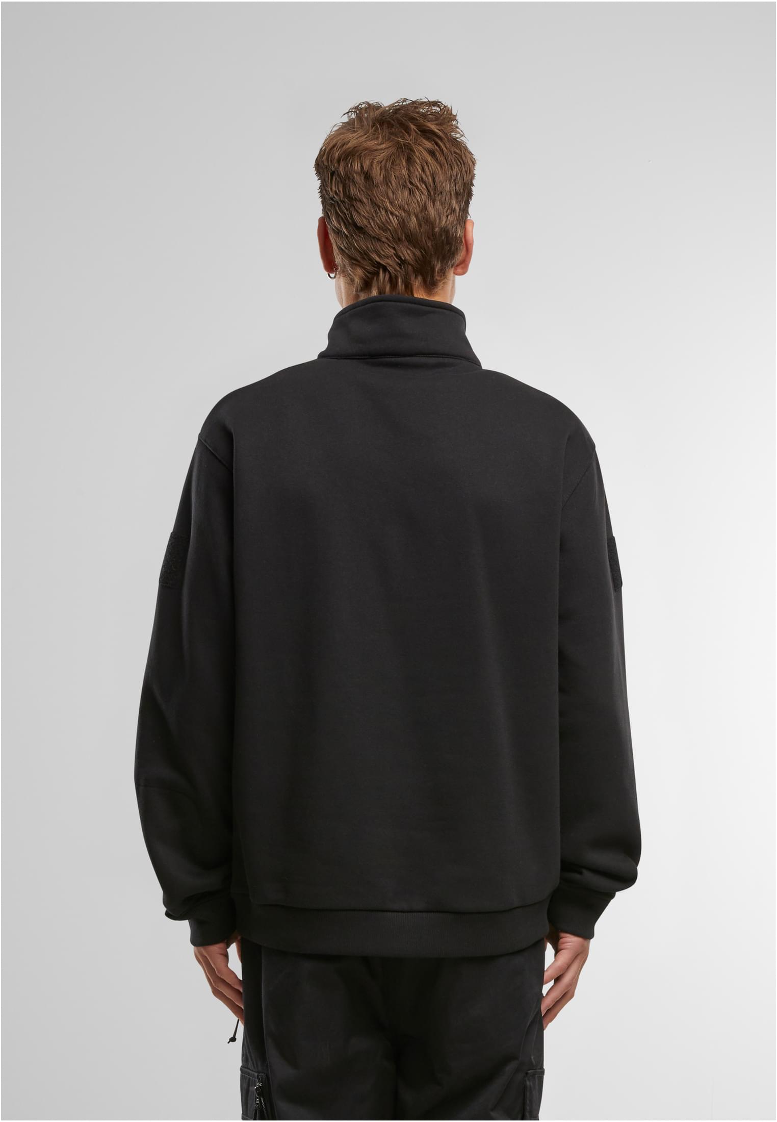 En man visar baksidan av en svart B Tactical Sweat Troyer.