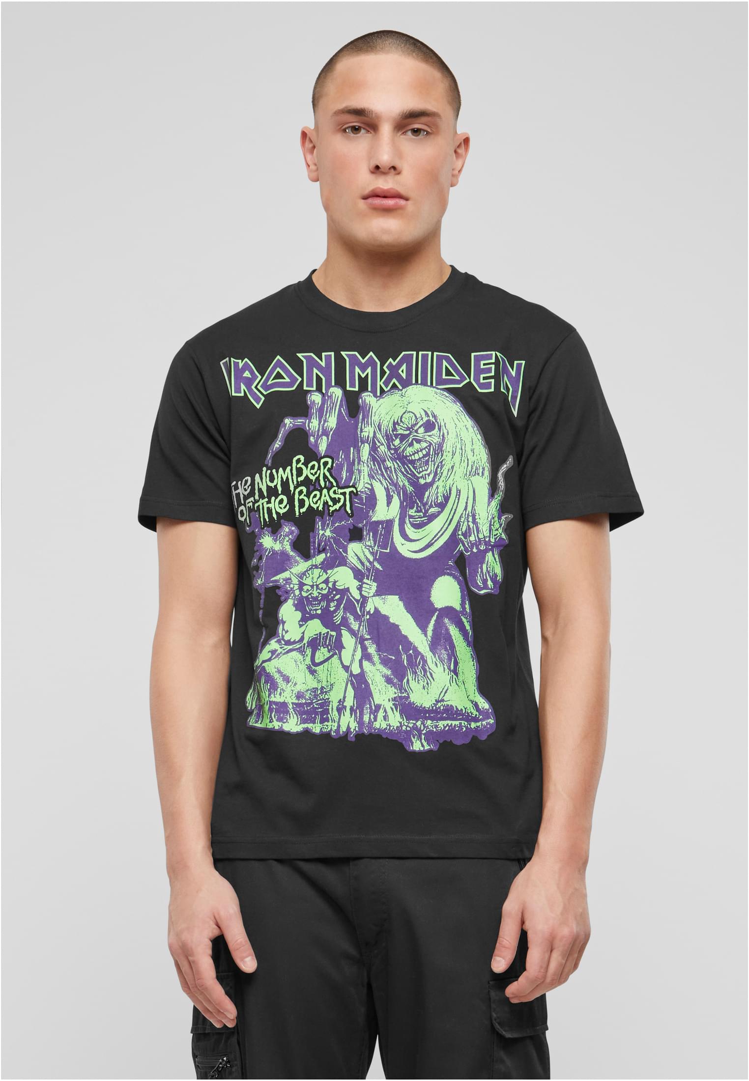 En manlig modell visar framsidan av en svart t-shirt med ett Iron Maiden 'The Number of the Beast'-tryck i grönt och lila.