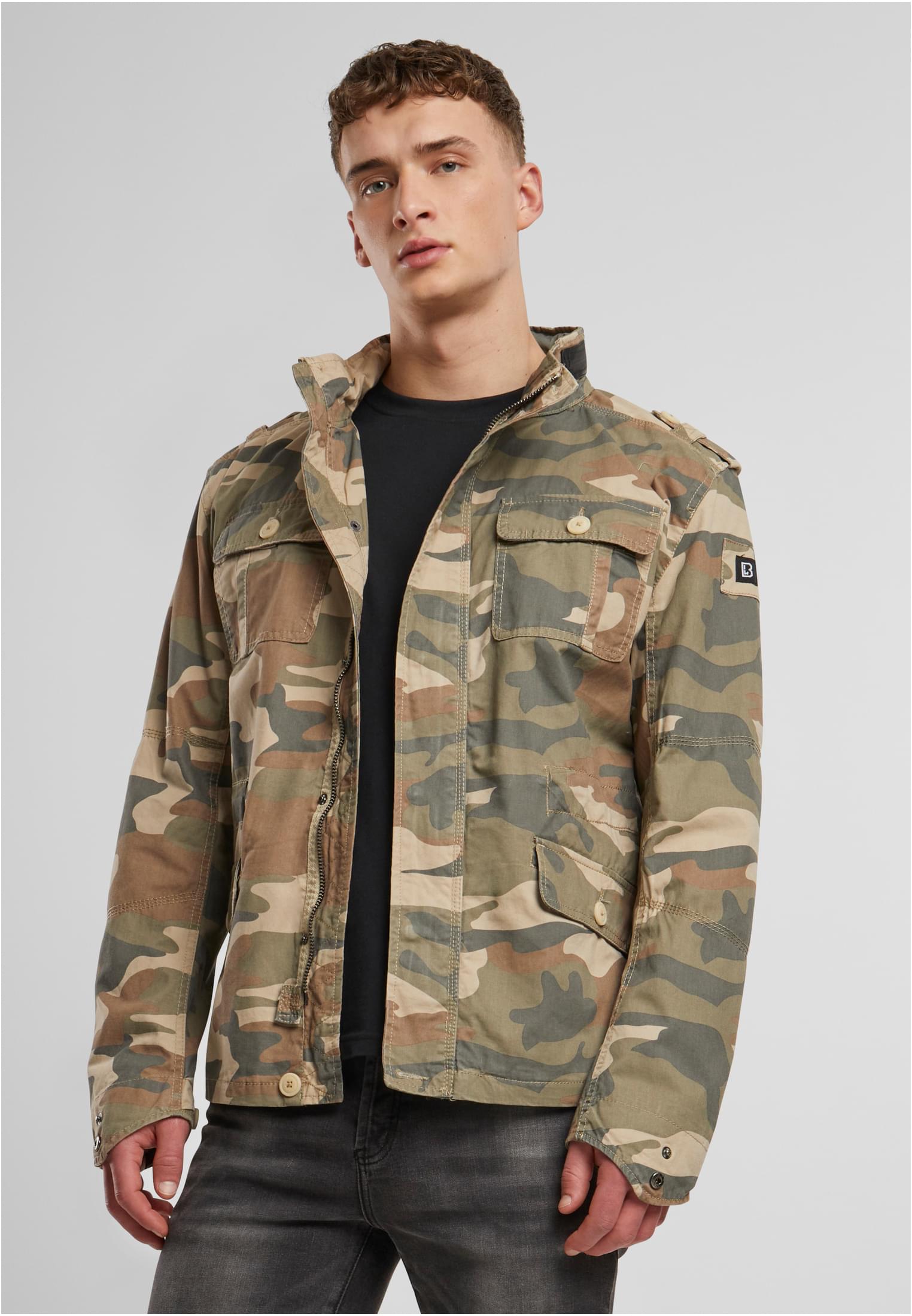 En man visar framsidan av B Britannia Jacket i kamouflagemönster.