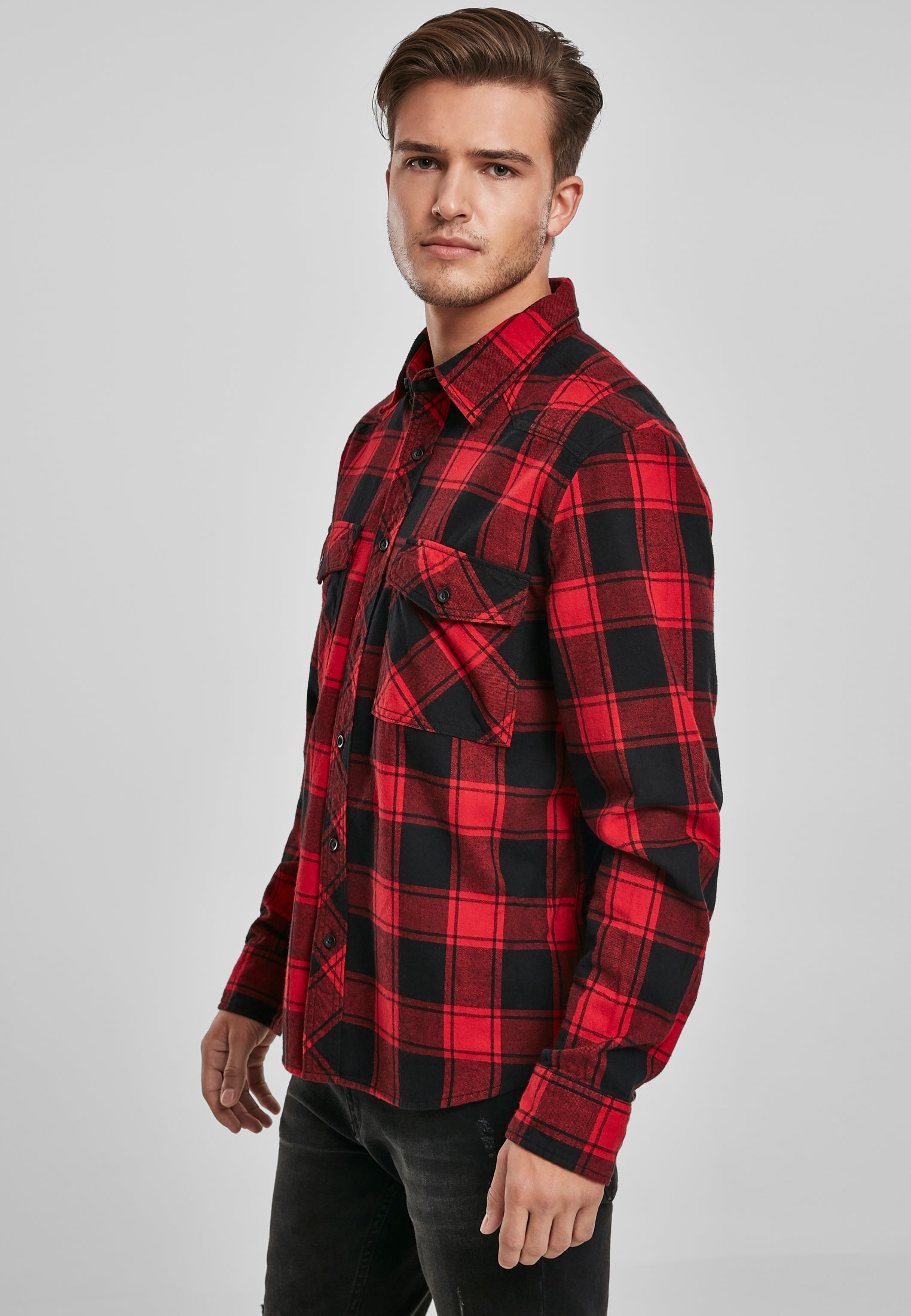 En man visar upp en röd och svart rutig skjorta med långa ärmar och bröstfickor.