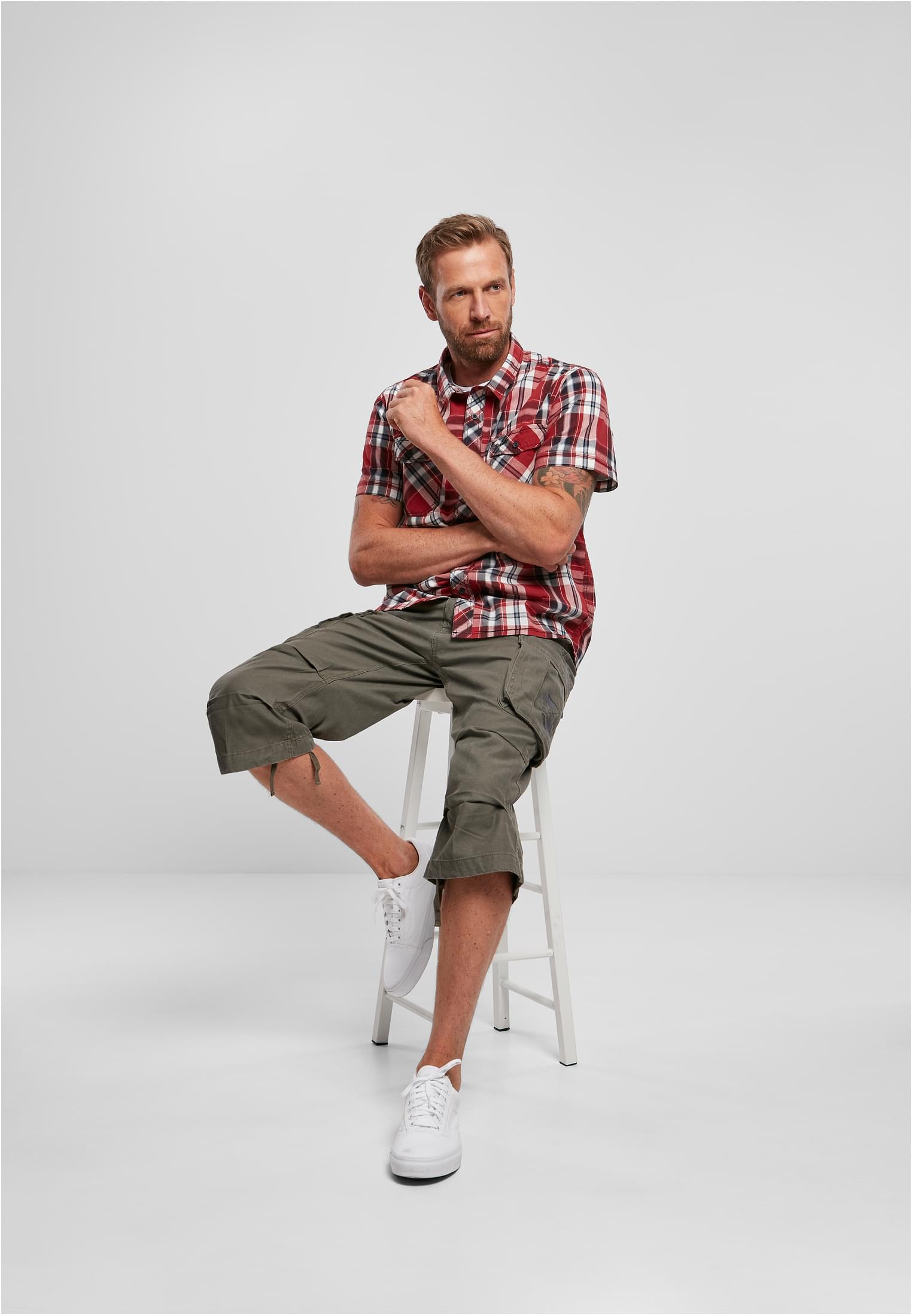 En man som sitter på en pall bär en kortärmad rödrutig B Roadstar-skjorta.