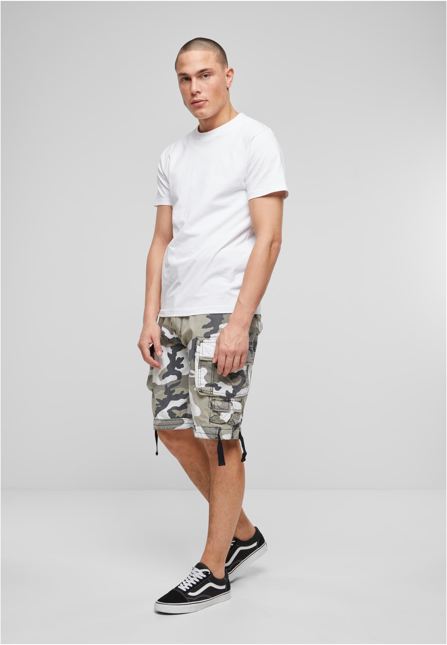 Manlig modell som bär B Savage Vintage Cargo Shorts i vit kamouflage, en vit t-shirt och svarta sneakers, fotograferad i en studio.