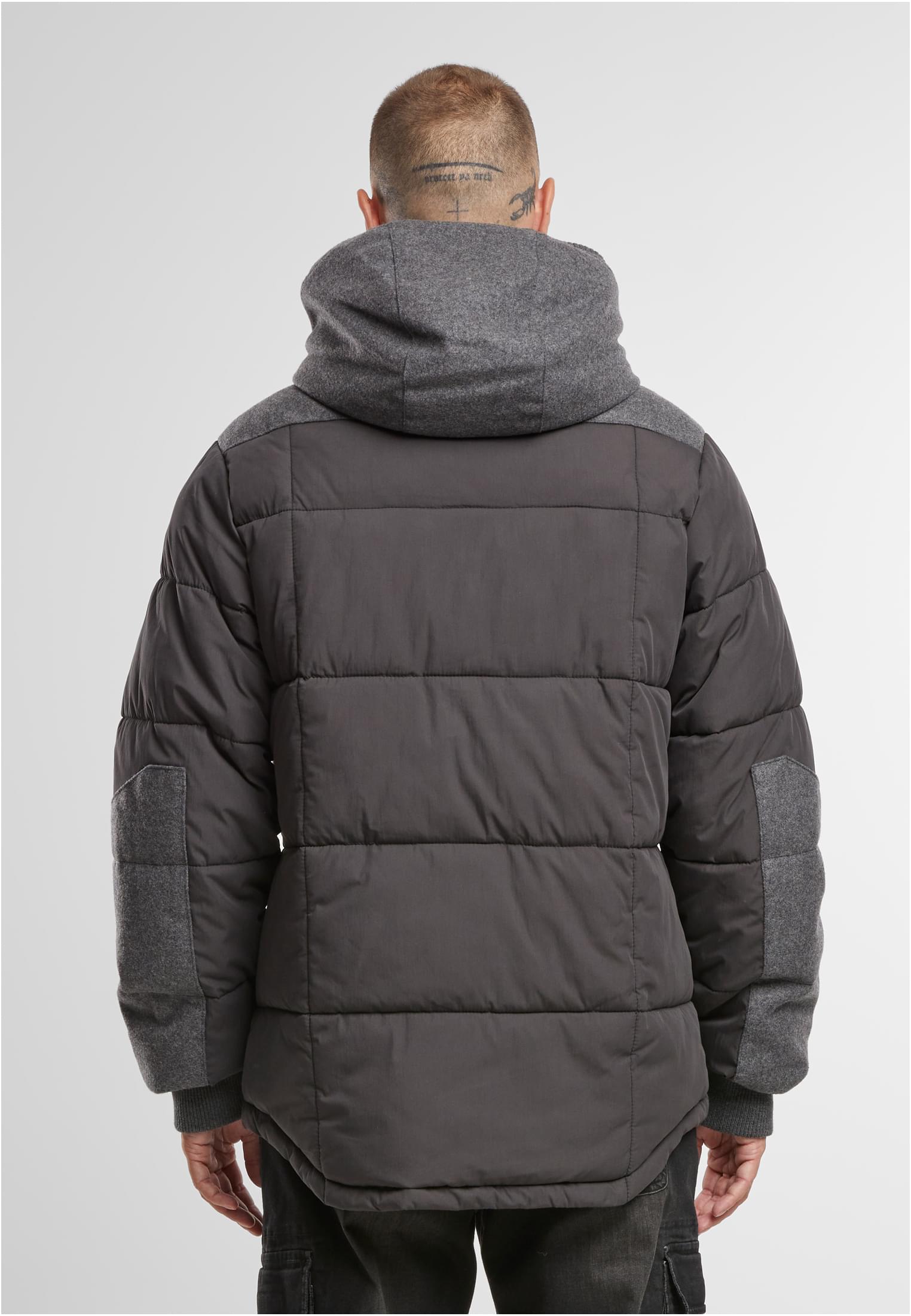 En man visar baksidan av en mörk, quiltad jacka med grå huva och axelpartier.