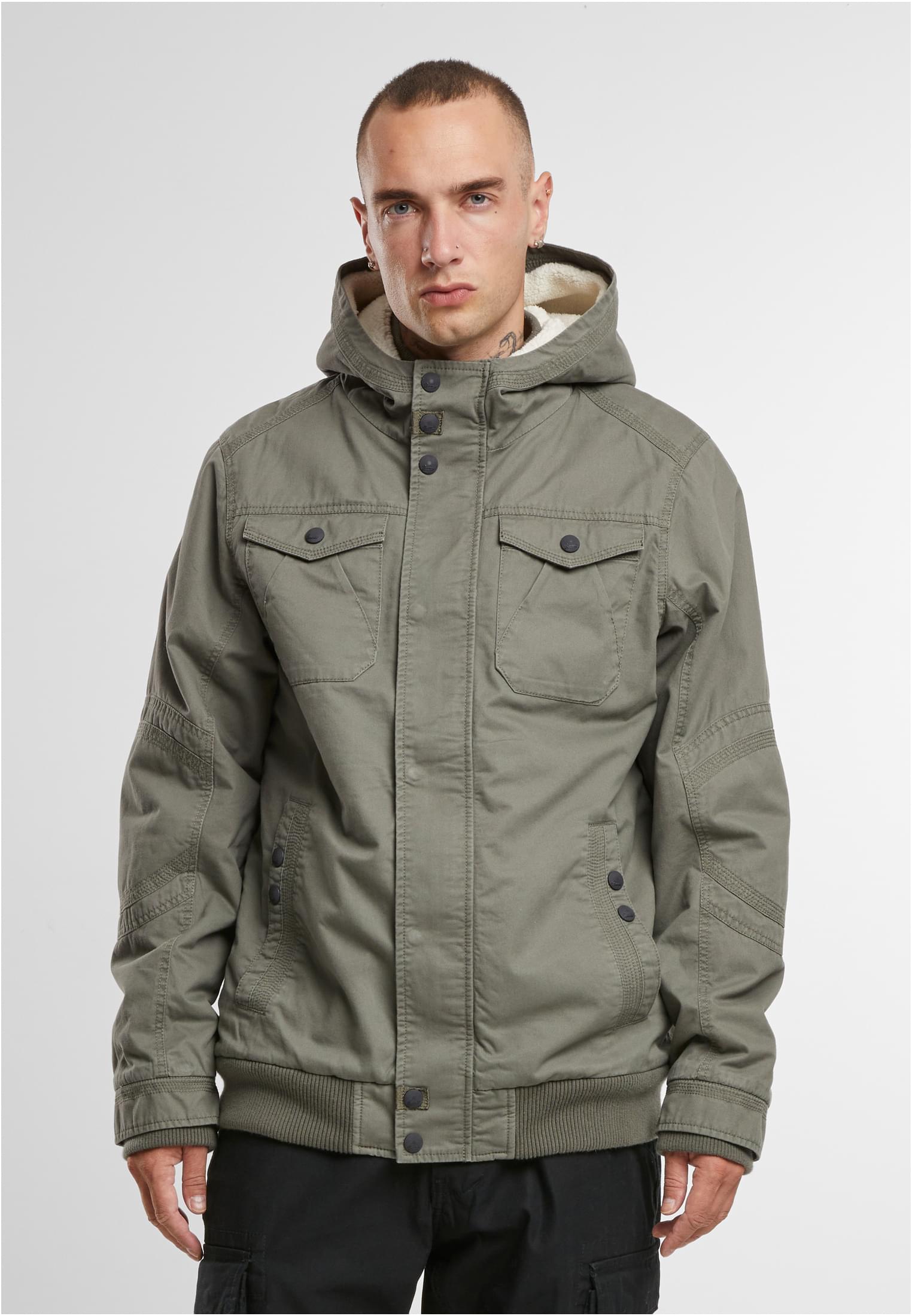 En man visar framsidan av den olivgröna B Meadow Jacket.