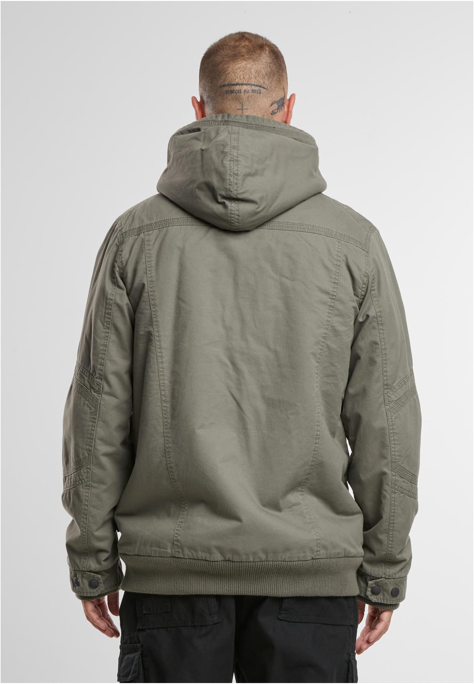 En man visar baksidan av B Meadow Jacket i olivgrönt.