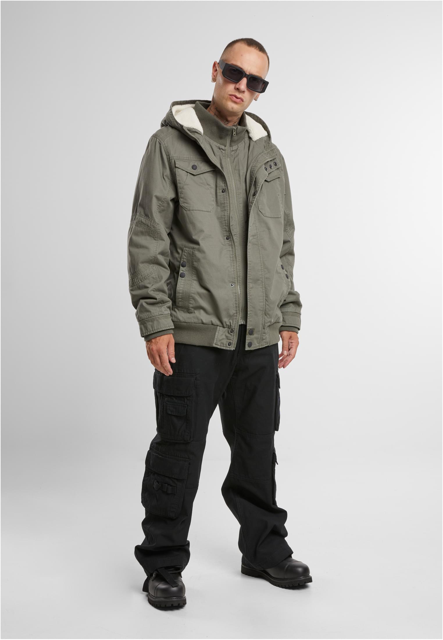 En man visar framsidan av en olivgrön B Meadow Jacket.