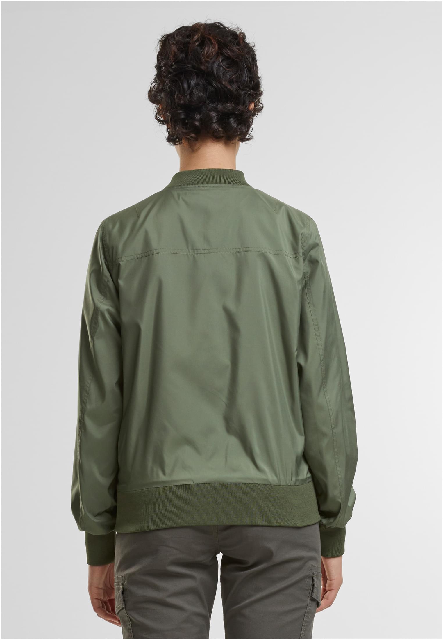 En kvinna visar baksidan av sin olivgröna B Jula Bomberjacka.