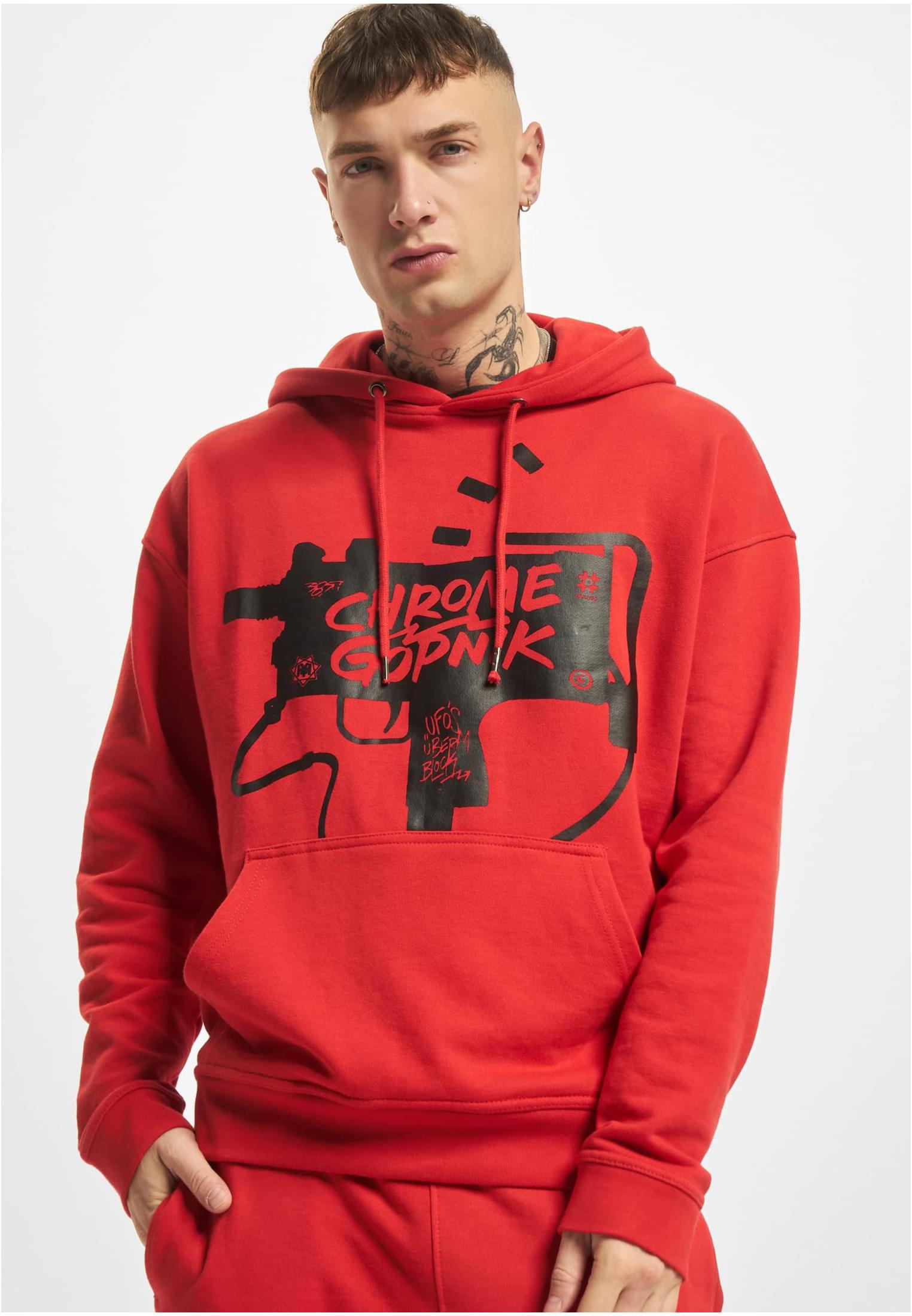 En man visar framsidan av en röd hoodie med ett stort svart grafiskt tryck.