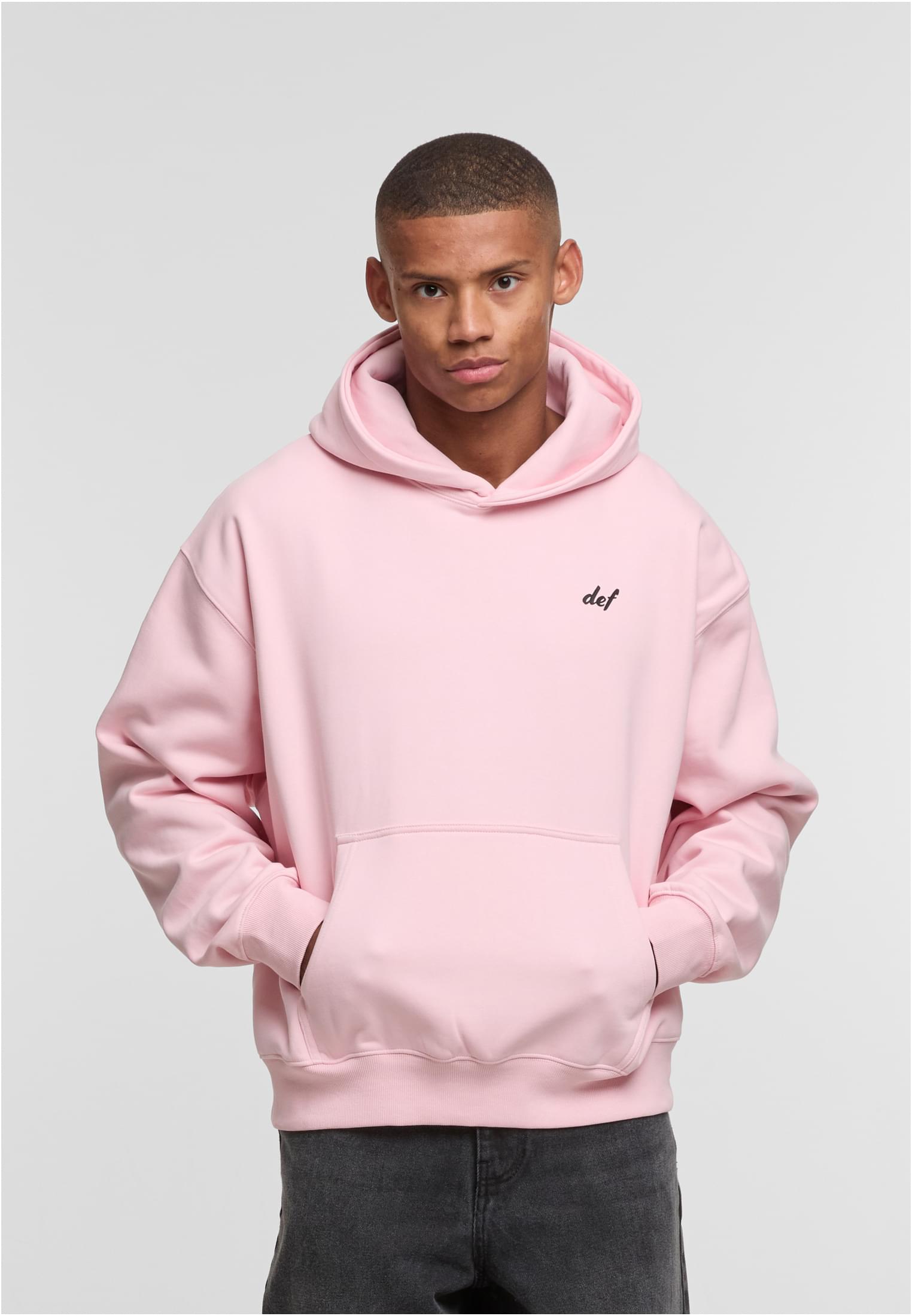 En manlig modell visar framsidan av en rosa DEF Visions-huvtröja med en liten svart logotyp på bröstet.