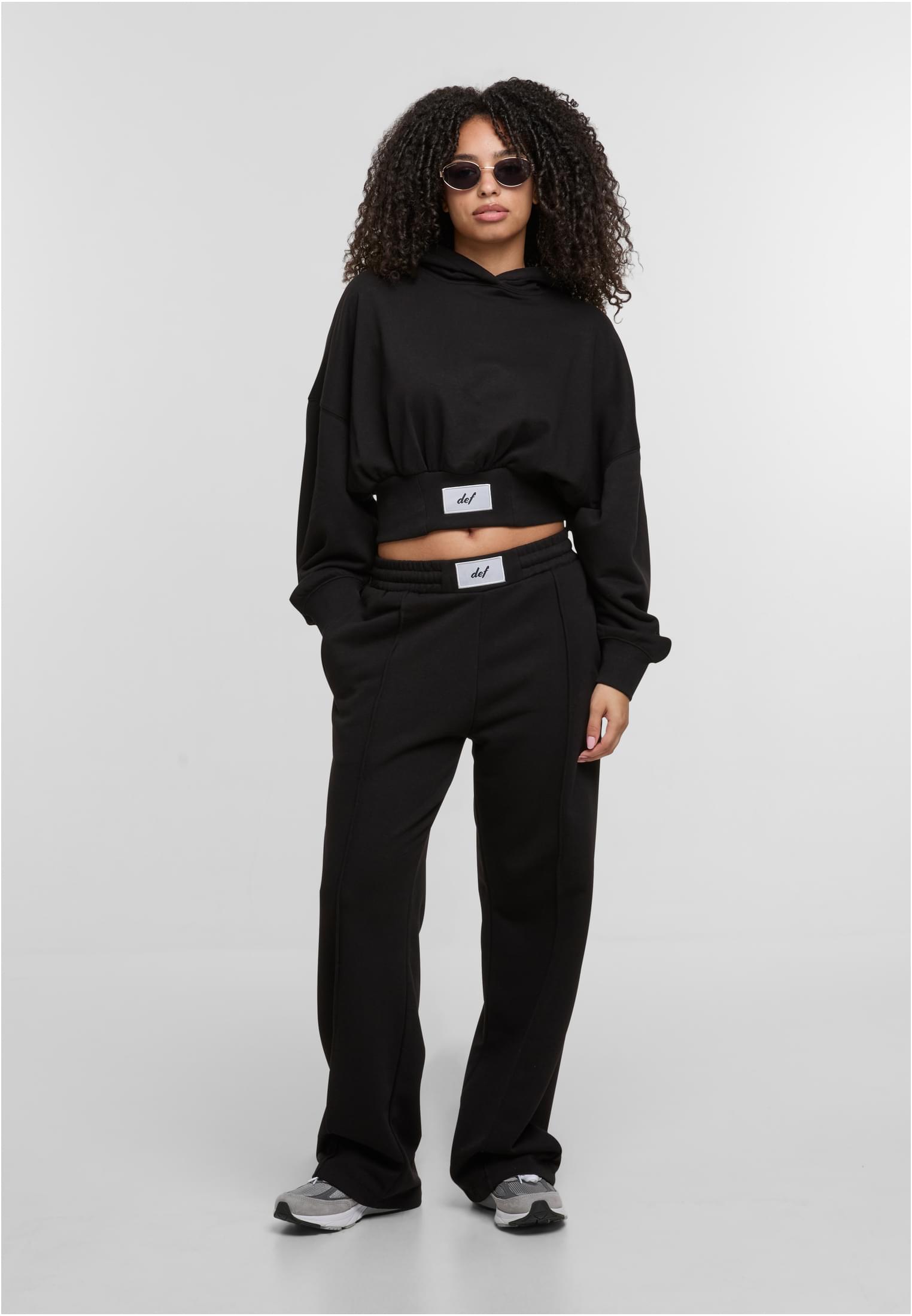 En kvinna poserar i en svart, kort DEF NICE Hoodie och matchande mjukisbyxor.