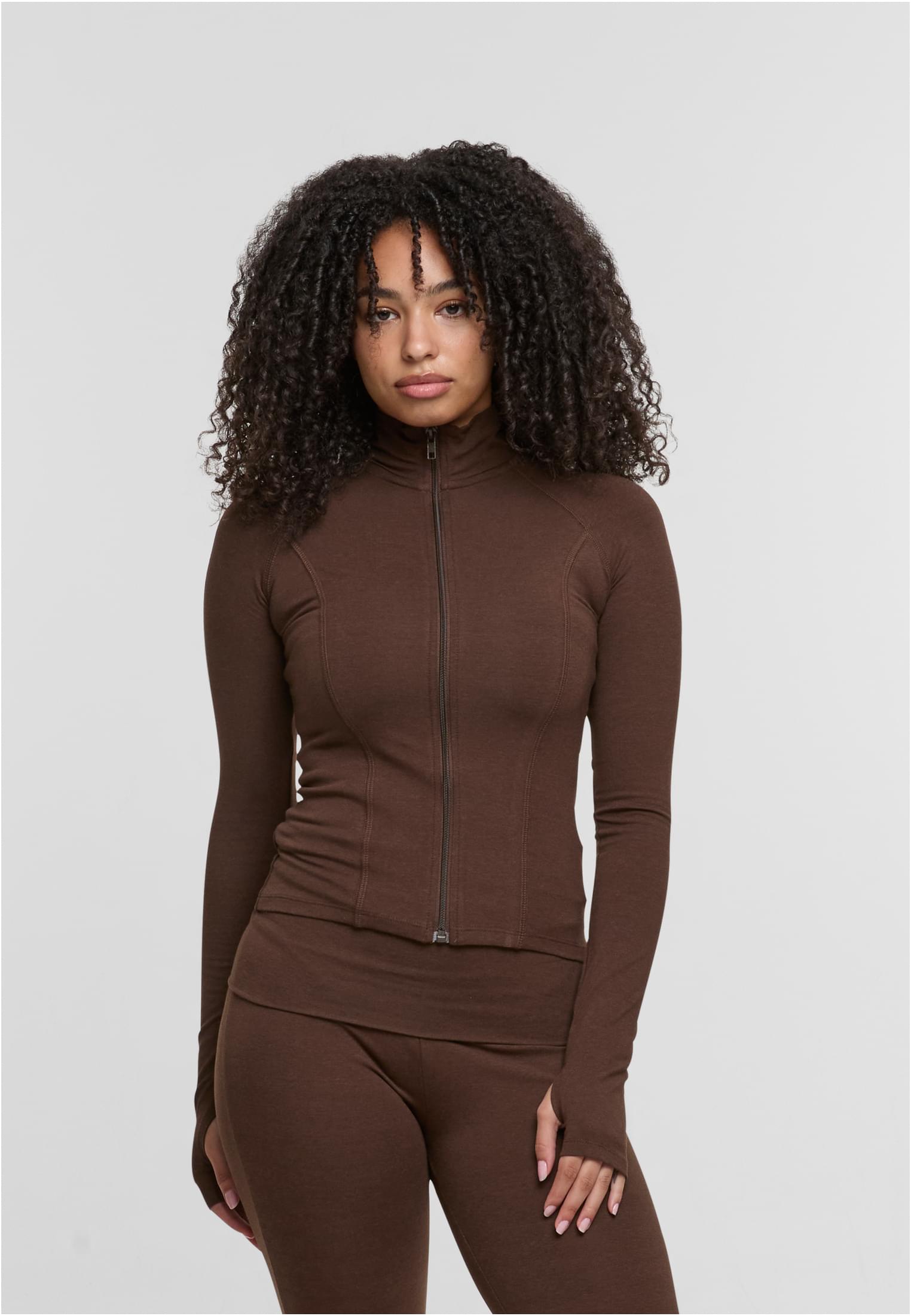 En kvinna visar framsidan av en brun, figurnära träningsjacka med dragkedja.