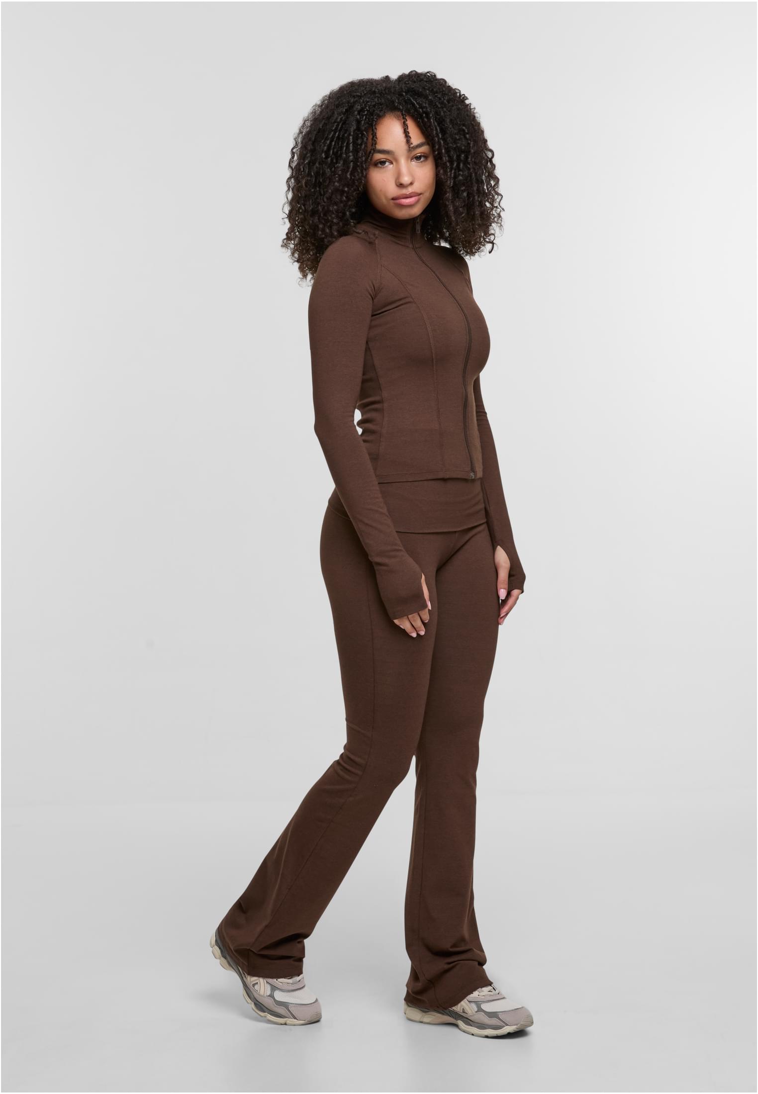 En kvinna visar upp en brun DEF GYM Track Jacket och matchande utsvängda träningsbyxor mot en vit bakgrund.