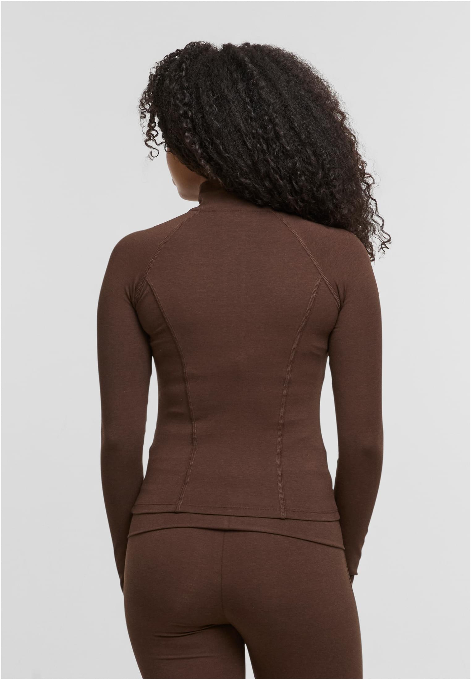 En kvinna visar baksidan av den bruna, långärmade träningsjackan DEF GYM.