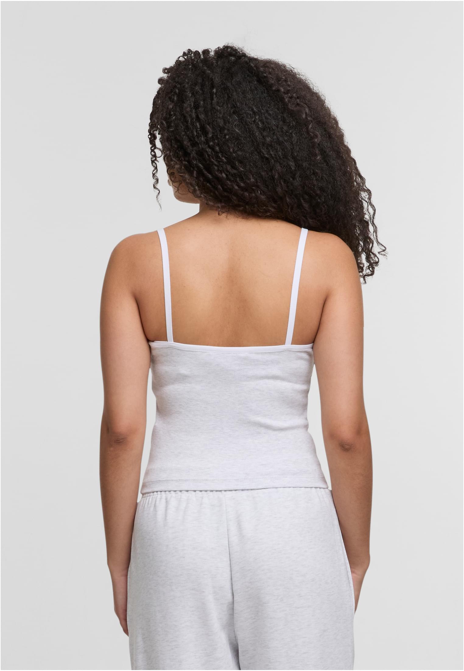 En kvinna visar baksidan av ett ljusgrått, ribbat linne med tunna axelband.