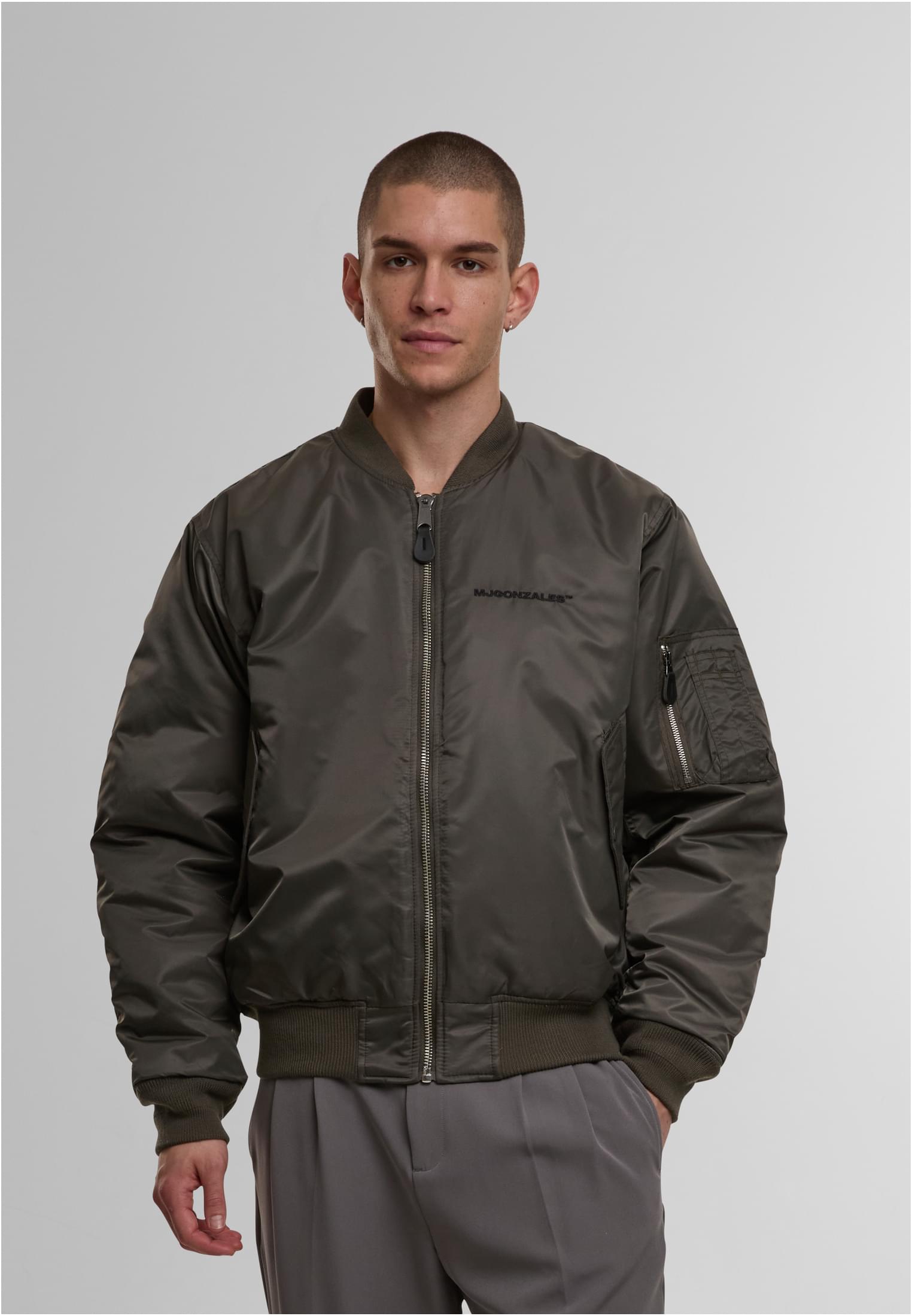 En man visar framsidan av MJG Bomberjackan i olivgrönt.