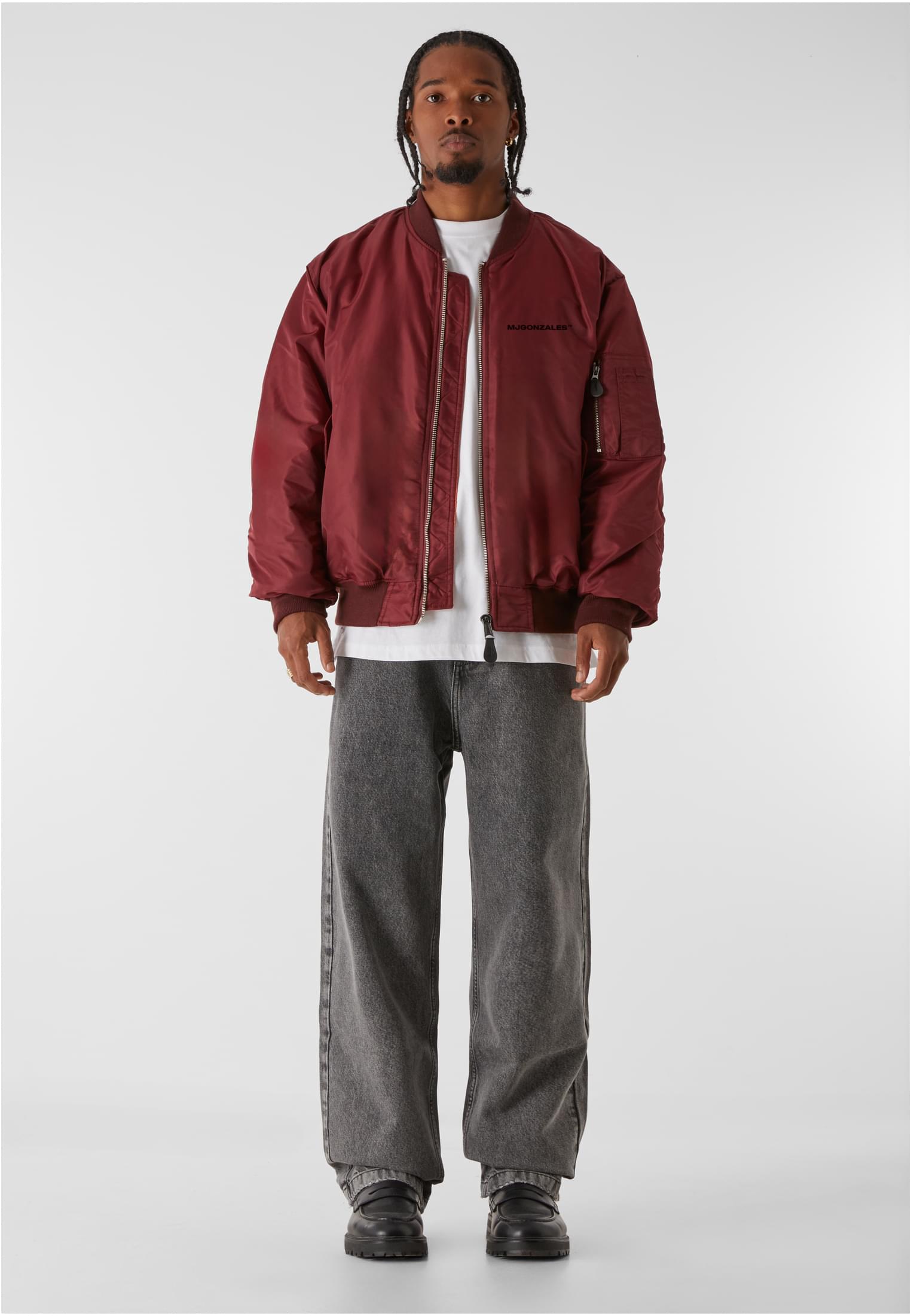 Helbild på en man som bär en röd MJG Bomber Jacket, en vit t-shirt och gråa jeans.