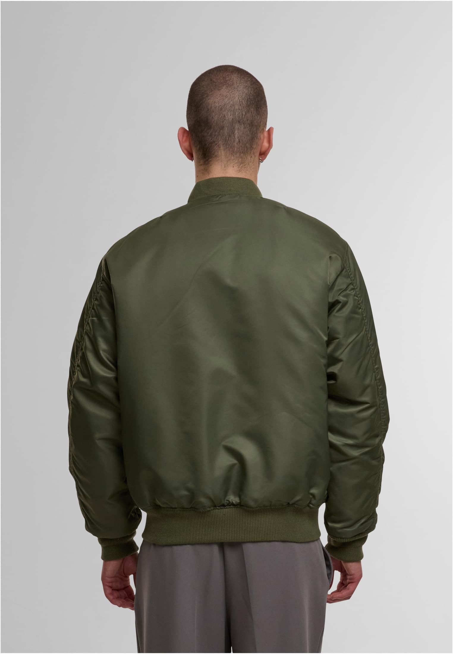 En man visar baksidan av en olivgrön MJG Bomber Jacket.