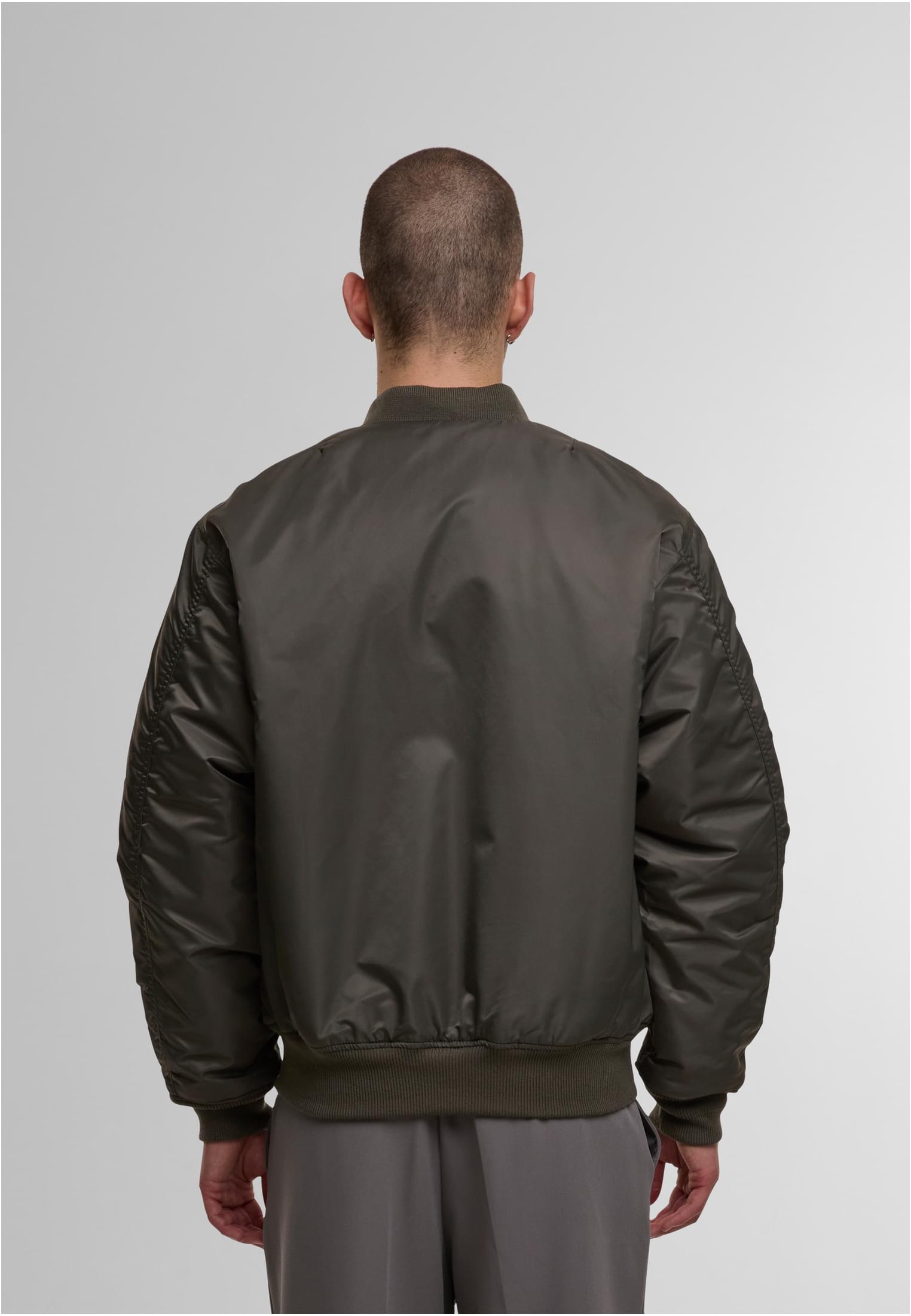 En man visar baksidan av en olivgrön MJG bomberjacka.