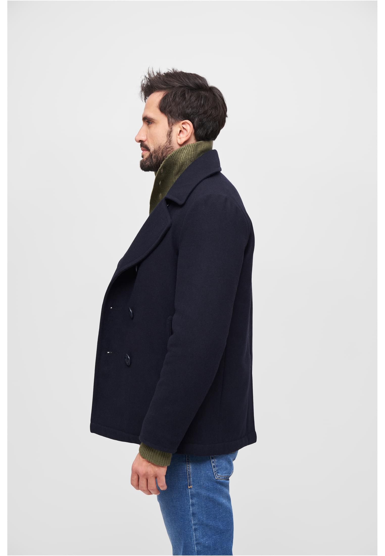 Sidoprofil av en man som bär en mörk B Pea Coat skepparkavaj över en grön polotröja och blåjeans.