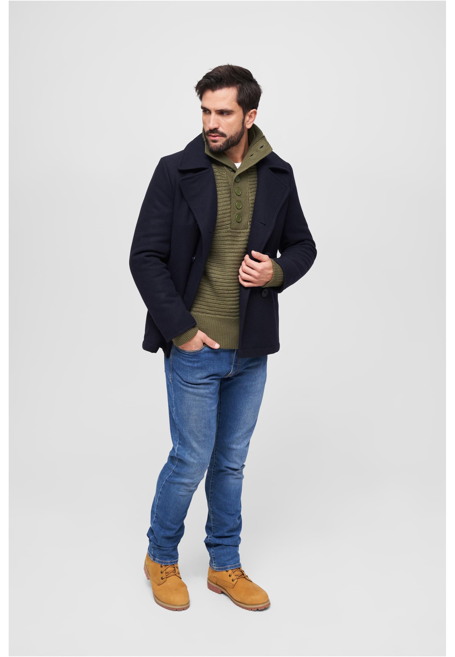 En man som bär en mörk B Pea Coat skepparkavaj, stylad med en olivgrön tröja, blå jeans och bruna kängor.