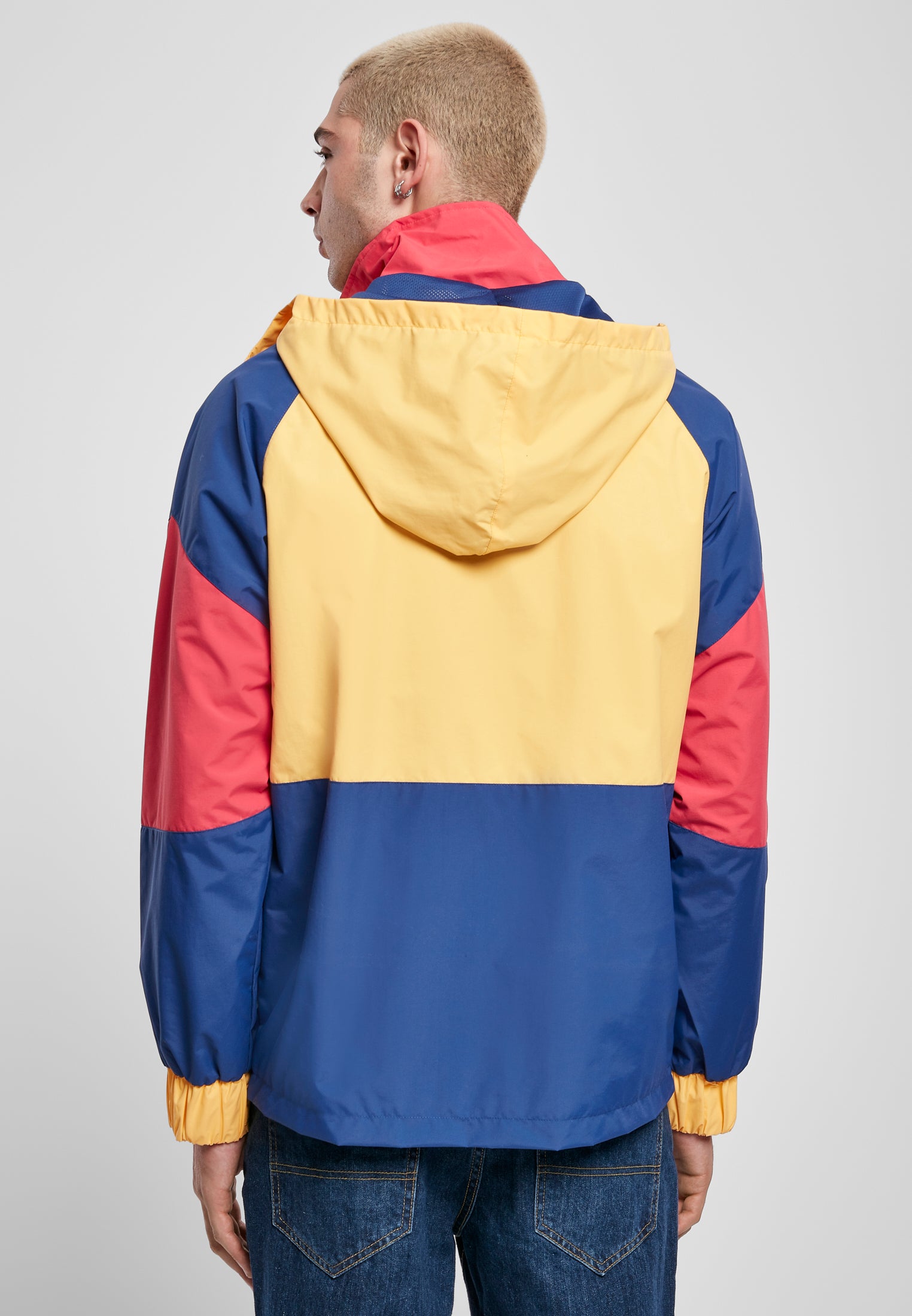 En man visar baksidan av en flerfärgad jacka med huva i färgerna gult, blått och rött.