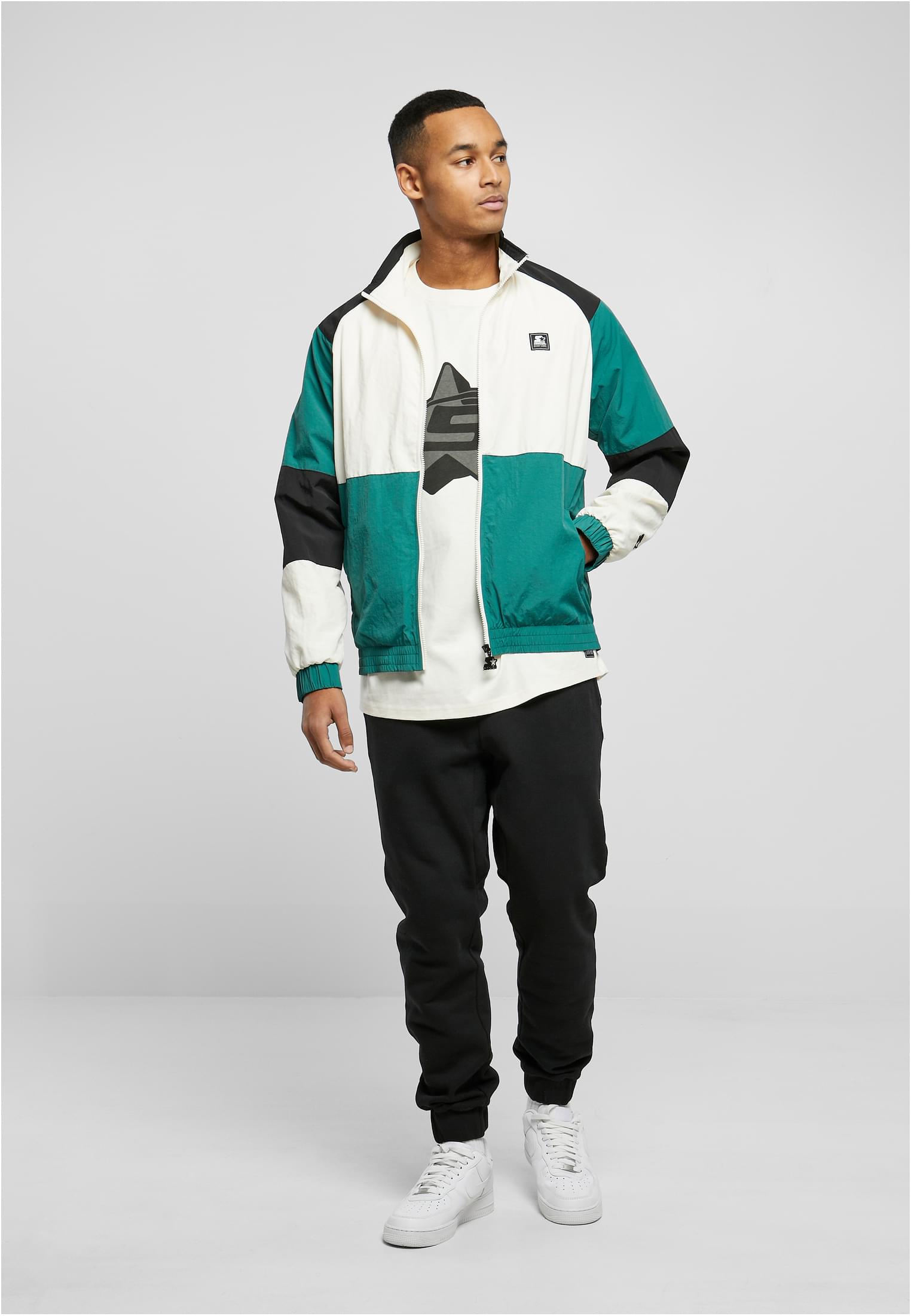 En man som bär en grön, vit och svart retrojacka med färgblock, kombinerad med svarta byxor och vita sneakers.