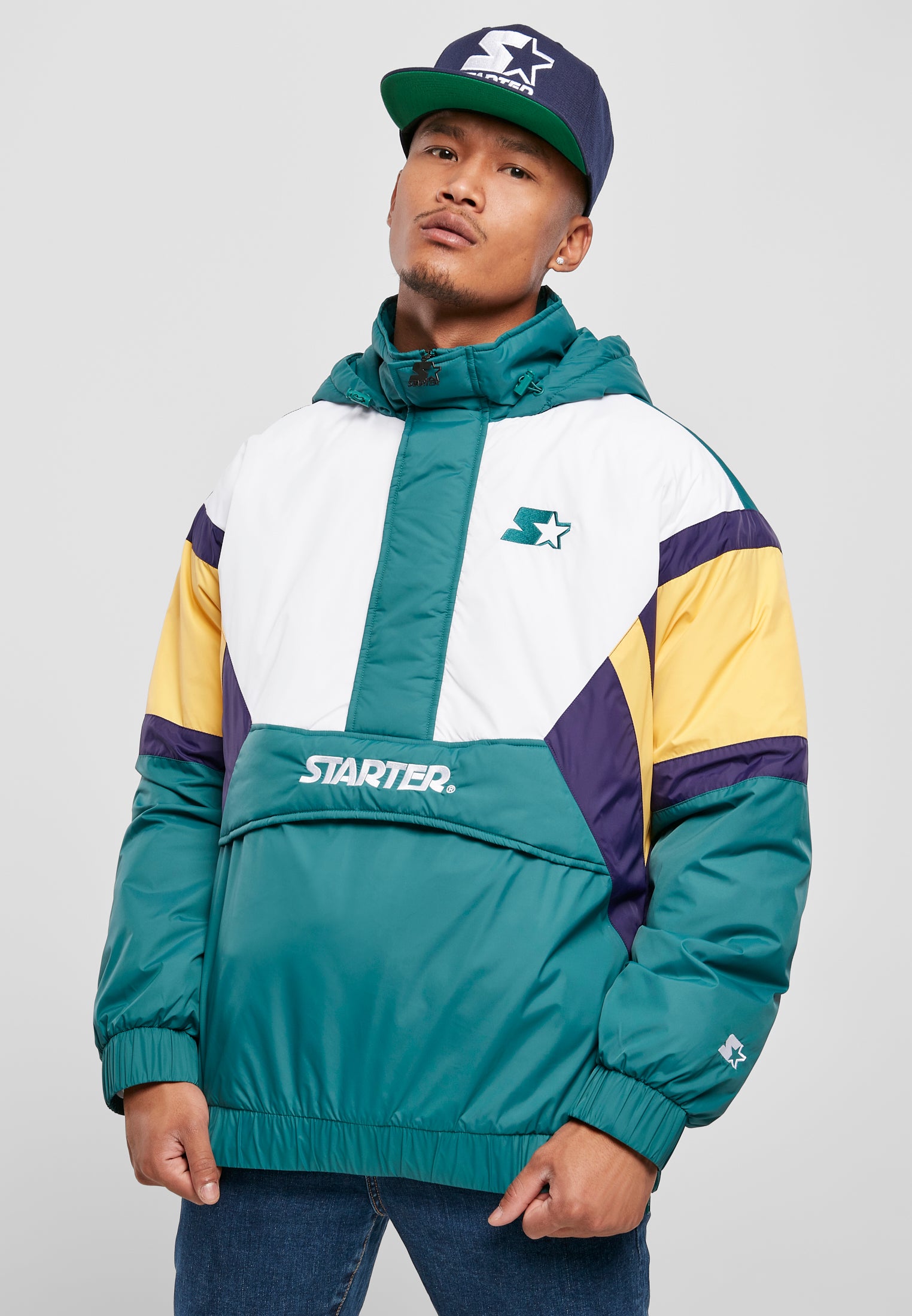 En man visar framsidan av en SBL Starter Color Block Half Zip Retro Jacket i grönt, vitt, gult och lila.
