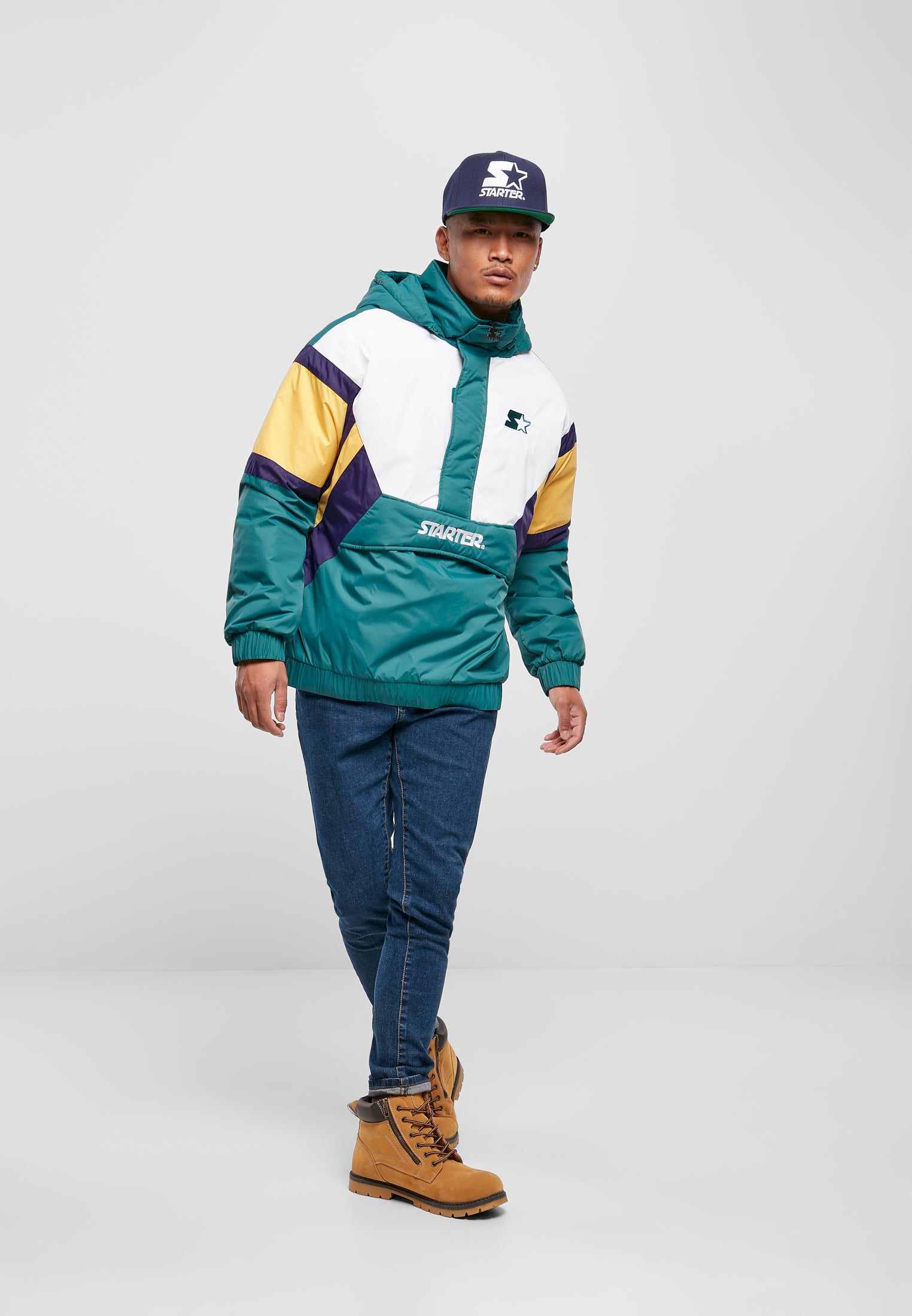 En man som bär den färgblockerade SBL Starter retrojackan i grönt, lila, gult och vitt, tillsammans med blå jeans och en keps.