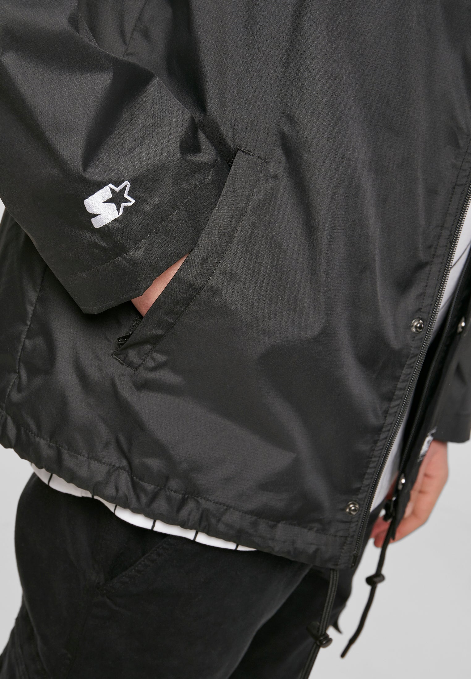 Närbild på en svart SBL Starter Coach Jacket, som visar sidofickan och den vita Starter-logotypen.