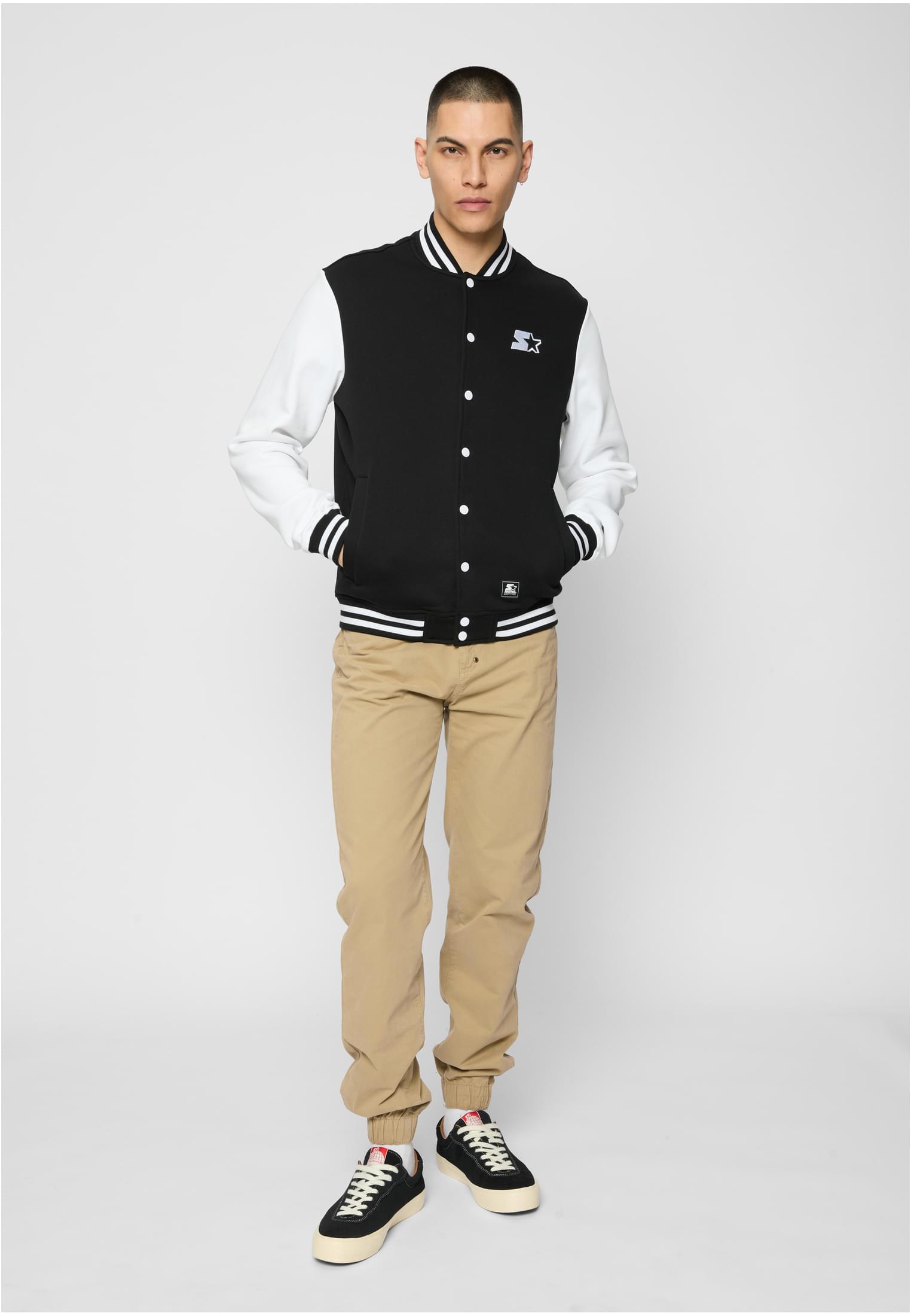 En man visar framsidan av en svart collegejacka med vita ärmar.