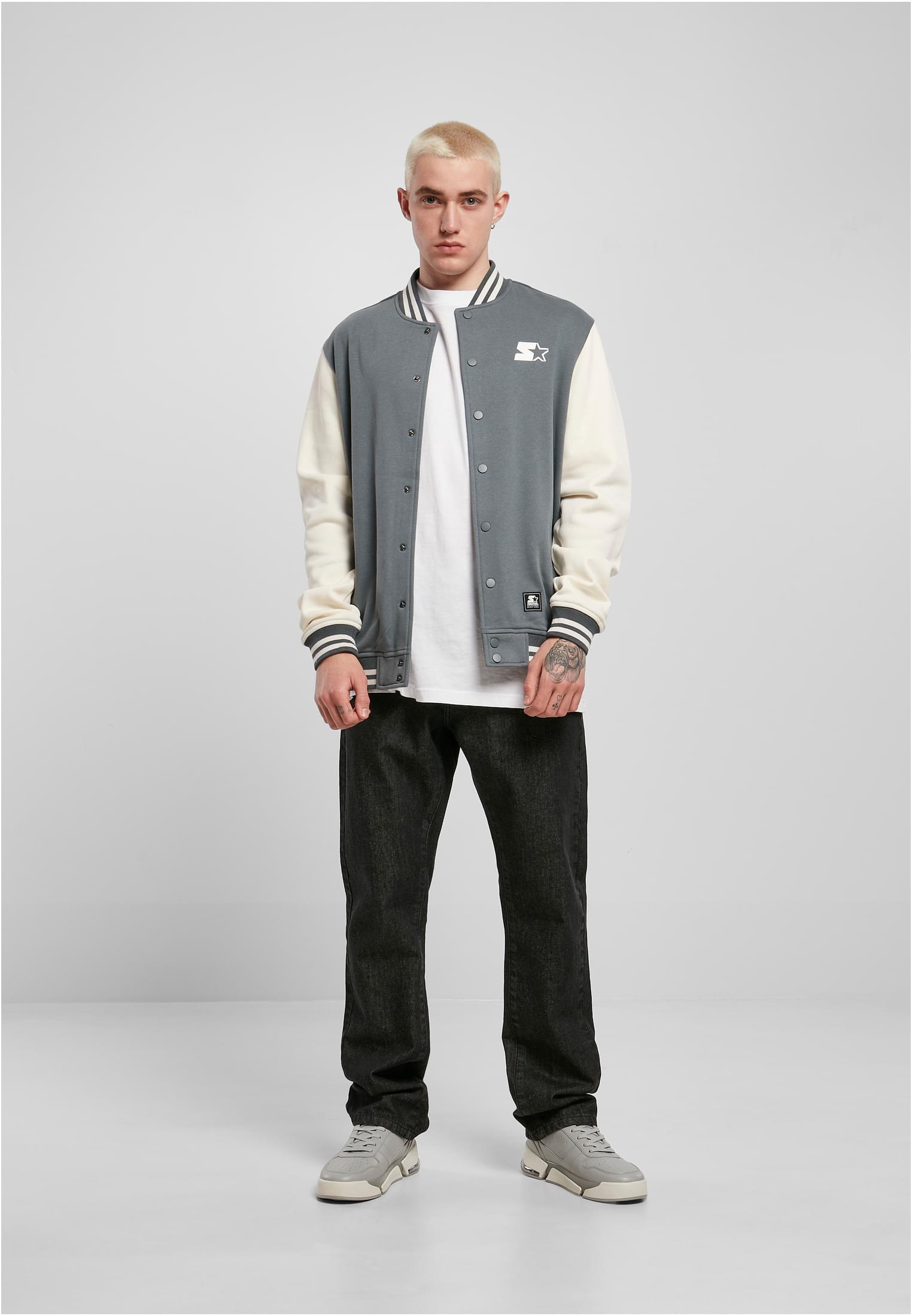 En man bär en grå SBL Starter College Fleece Jacket med benvita ärmar, en vit t-shirt, svarta jeans och grå sneakers.