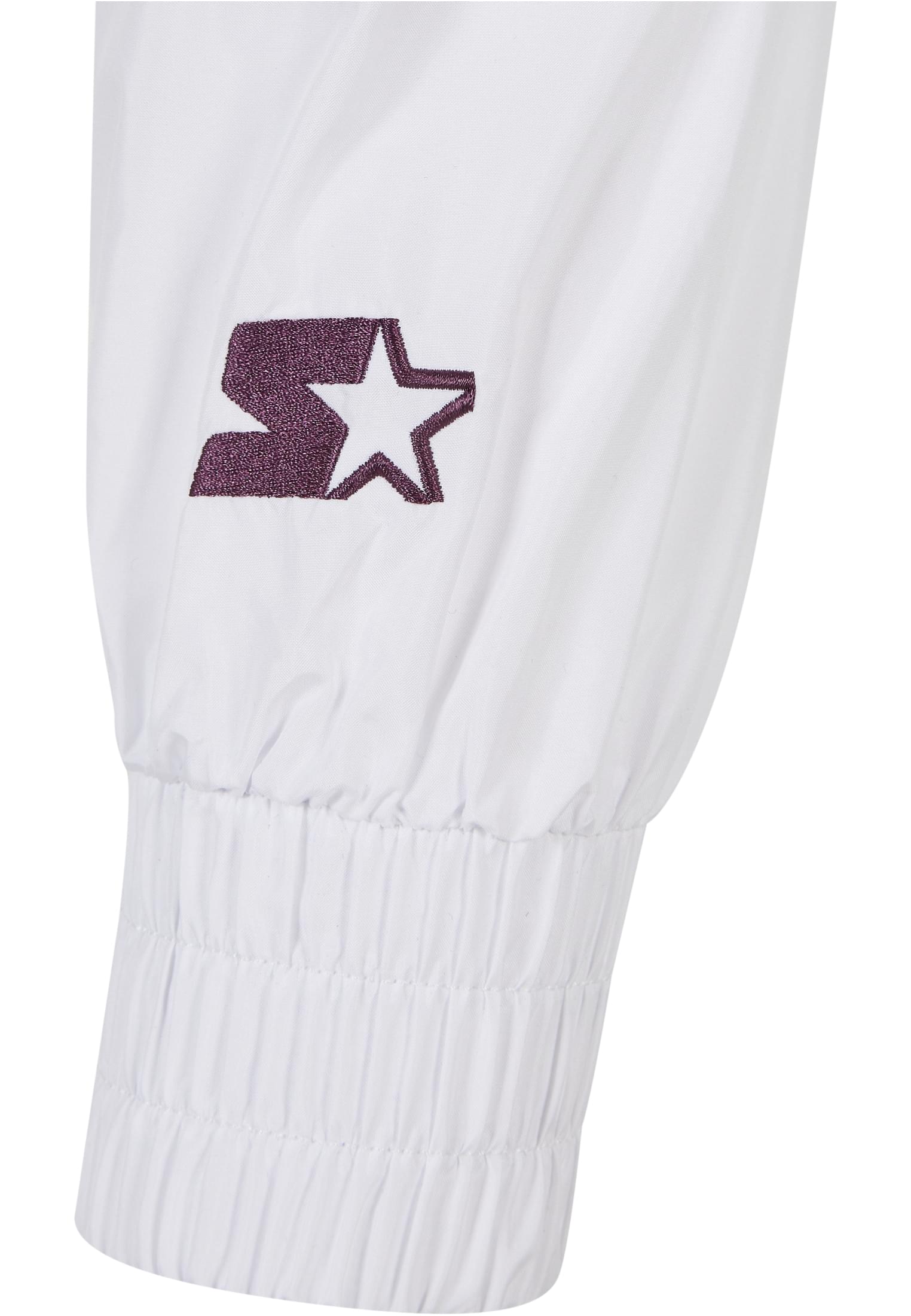 Detaljbild av den lila broderade Starter-loggan på ärmen av en vit jacka med elastisk mudd.
