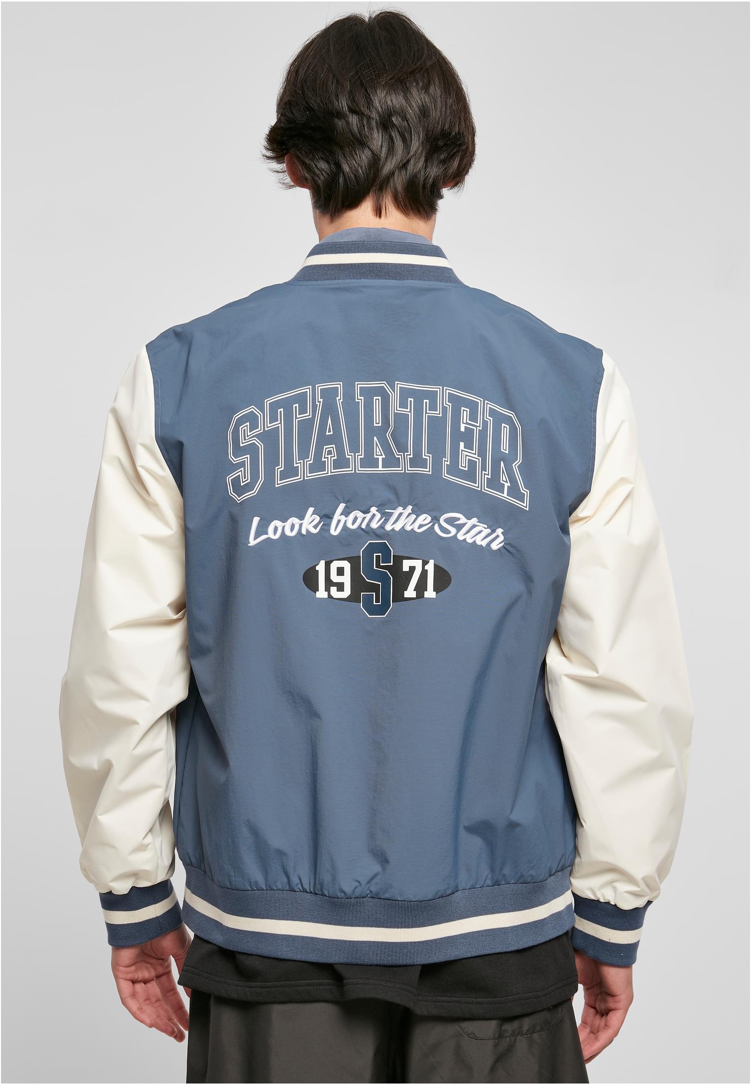 En man visar baksidan av sin blå och vita SBL Starter Nylon College Jacket, med en stor 'Starter'-logotyp tryckt på ryggen.