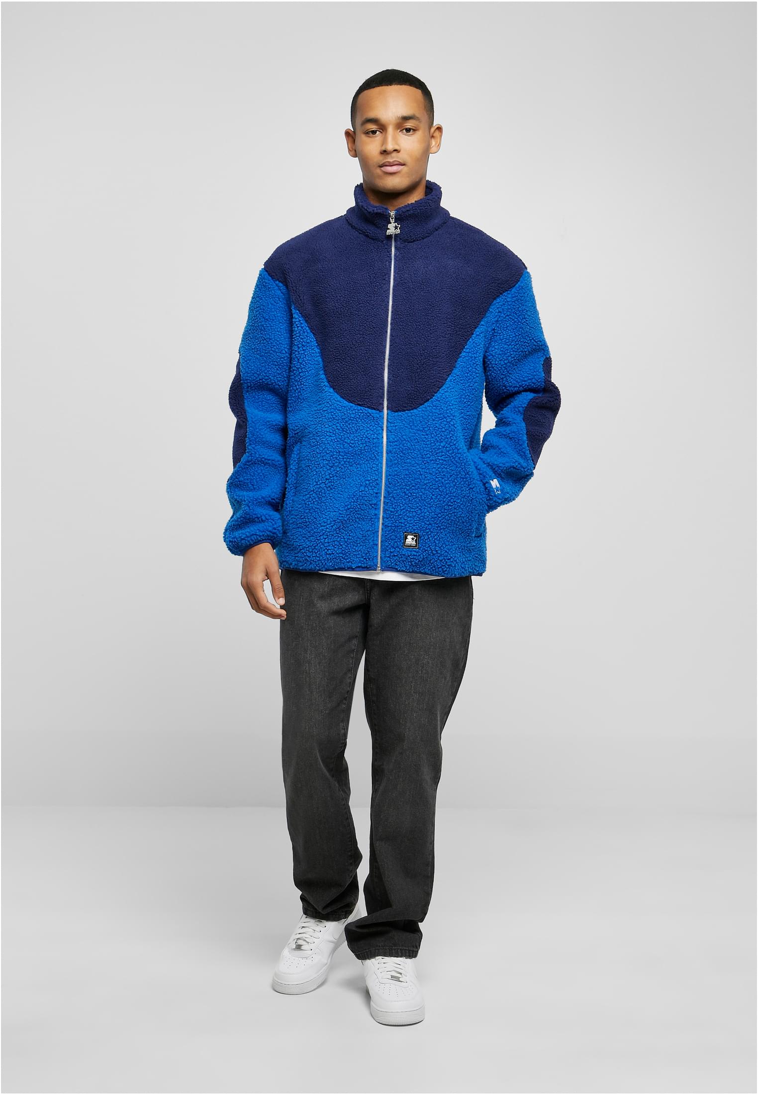 En man visar framsidan av den blå- och marinblåa SBL Starter Sherpa Fleece-jackan.