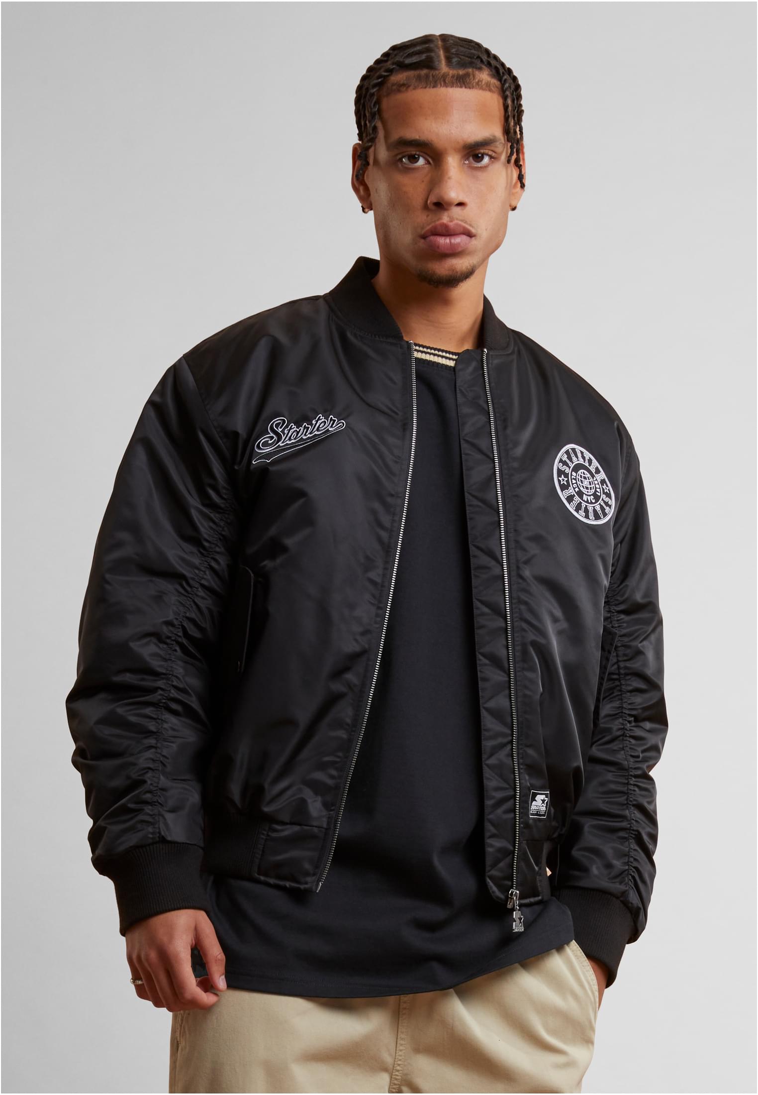 En man visar framsidan av en svart SBL Starter Patch Bomber jacket.