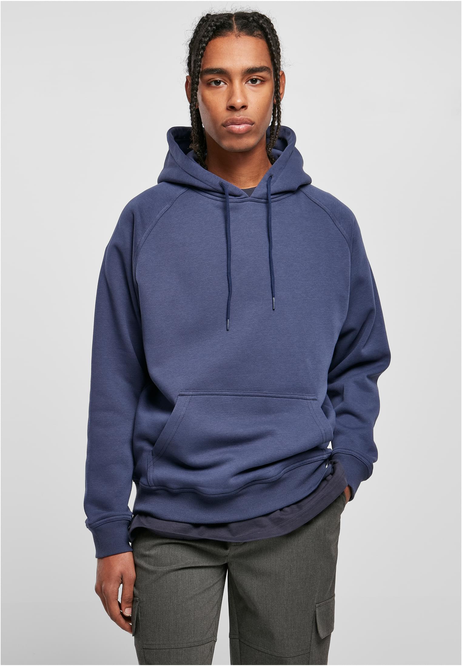 En manlig modell med flätat hår som bär en mörkblå UC Blank Hoody.