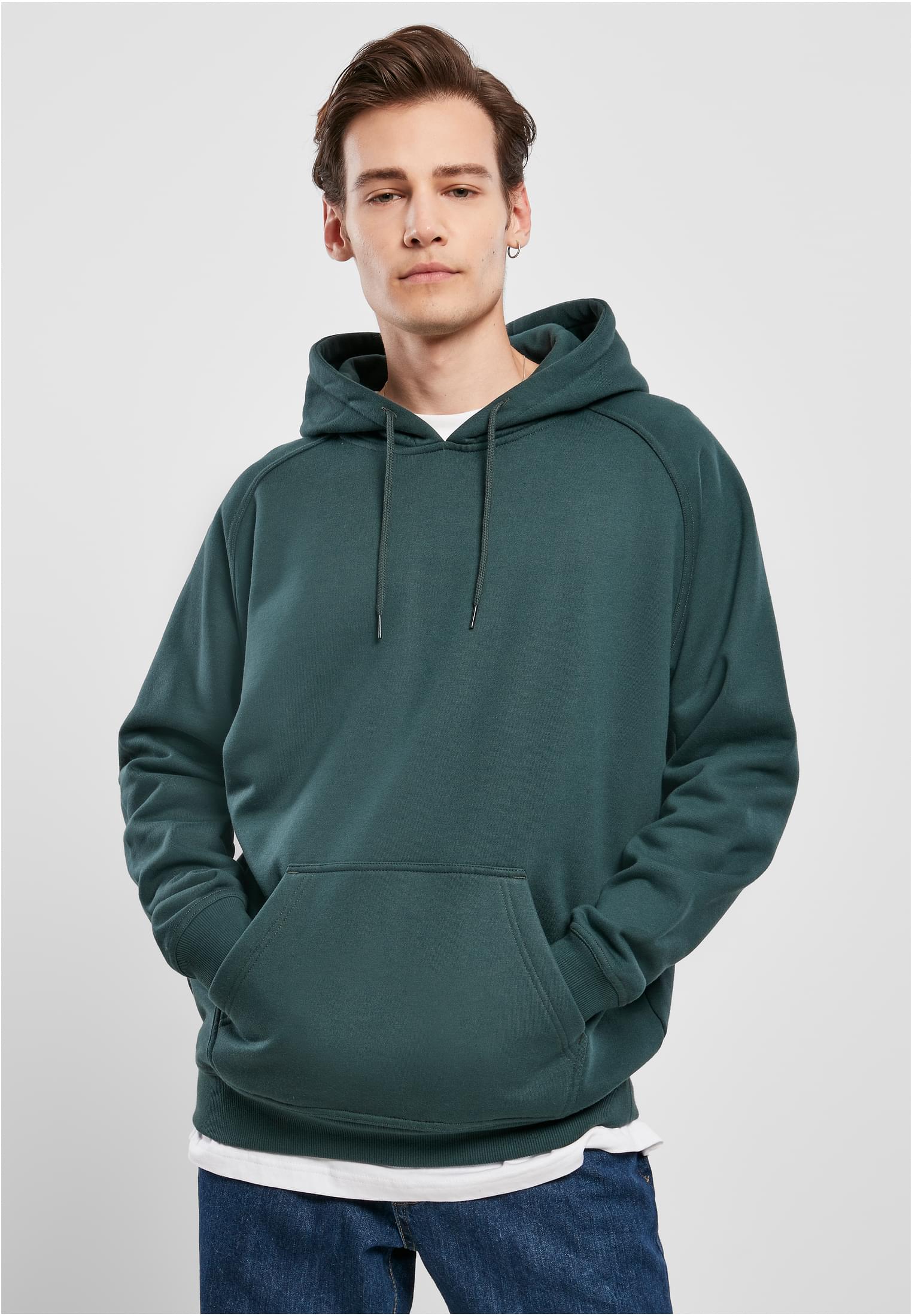 En man poserar framifrån i en mörkgrön UC Blank Hoody med händerna i kängurufickan.
