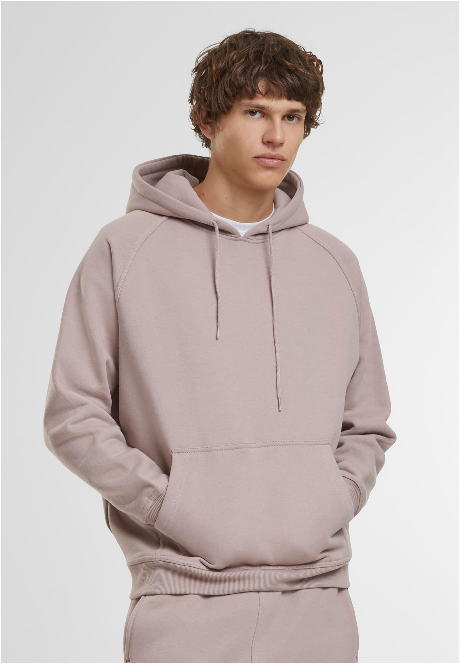 Manlig modell som bär en dammrosa UC Blank Hoody med händerna i kängurufickan, fotograferad framifrån mot en vit bakgrund.