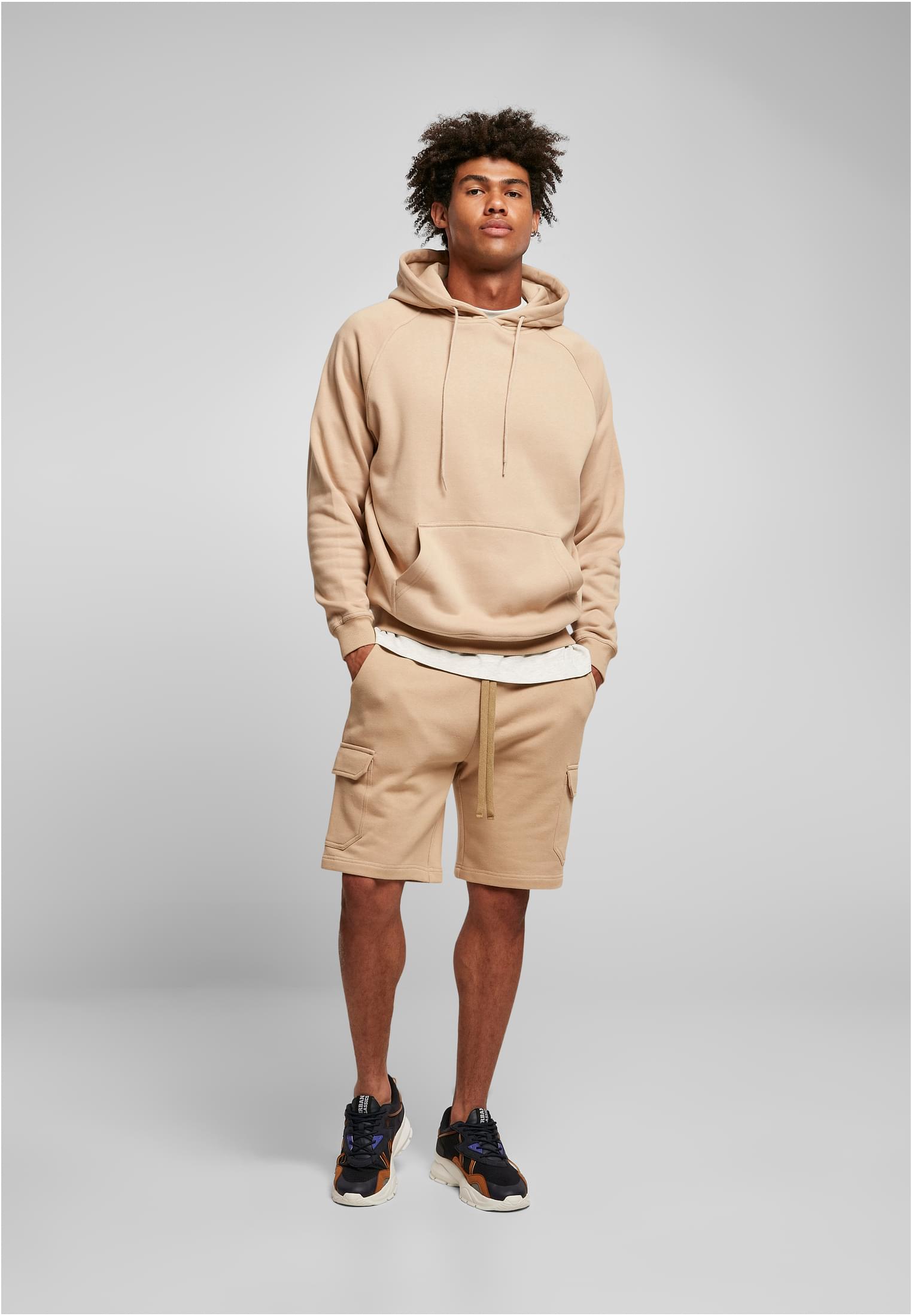 Manlig modell i en beige UC Blank Hoody, fotograferad framifrån mot en grå bakgrund.