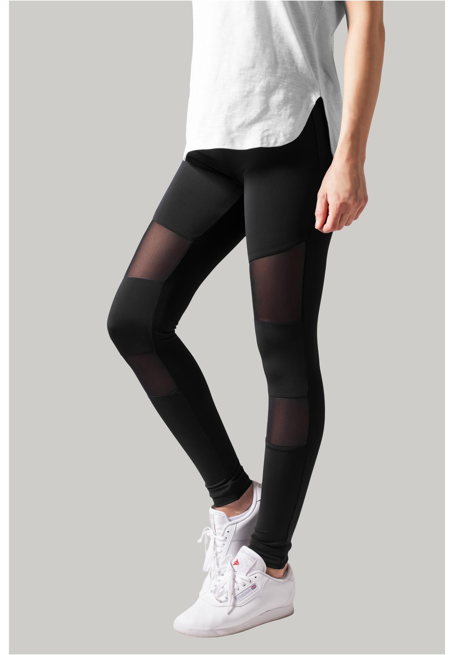 Närbild från sidan på en kvinna som bär svarta Ladies Tech Mesh Leggings med mesh-inlägg, kombinerat med en vit t-shirt och vita sneakers.