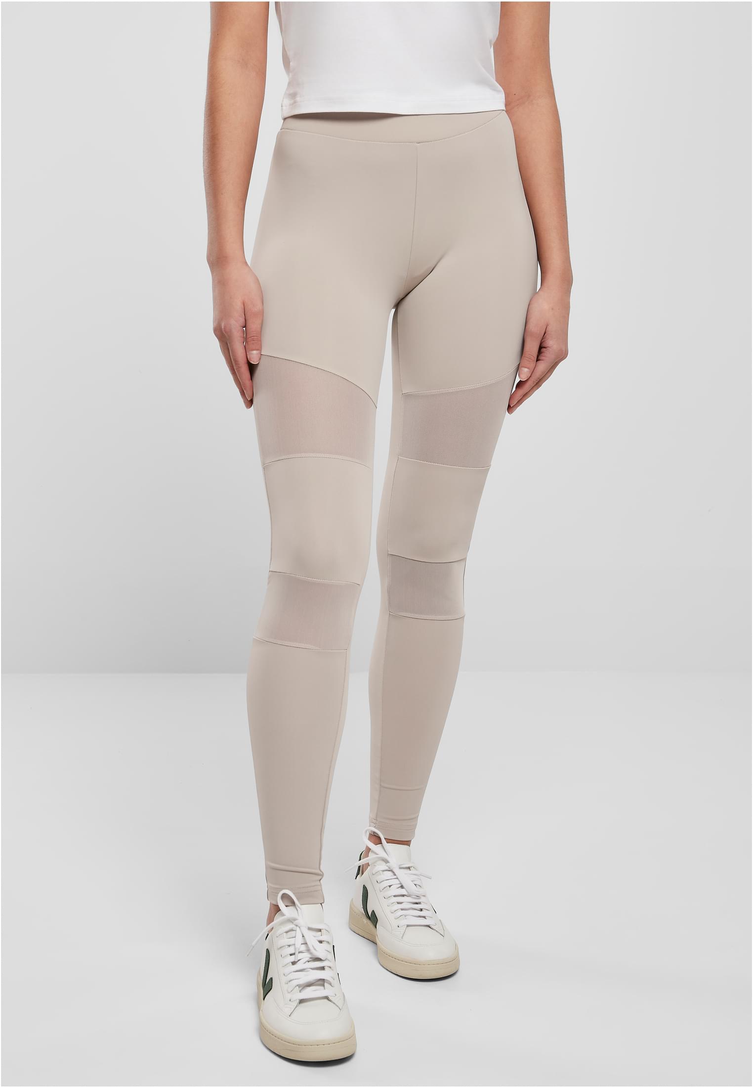 Framsida av en kvinna som bär Ladies Tech Mesh Leggings i varmgrått med nätpaneler över knän och lår.