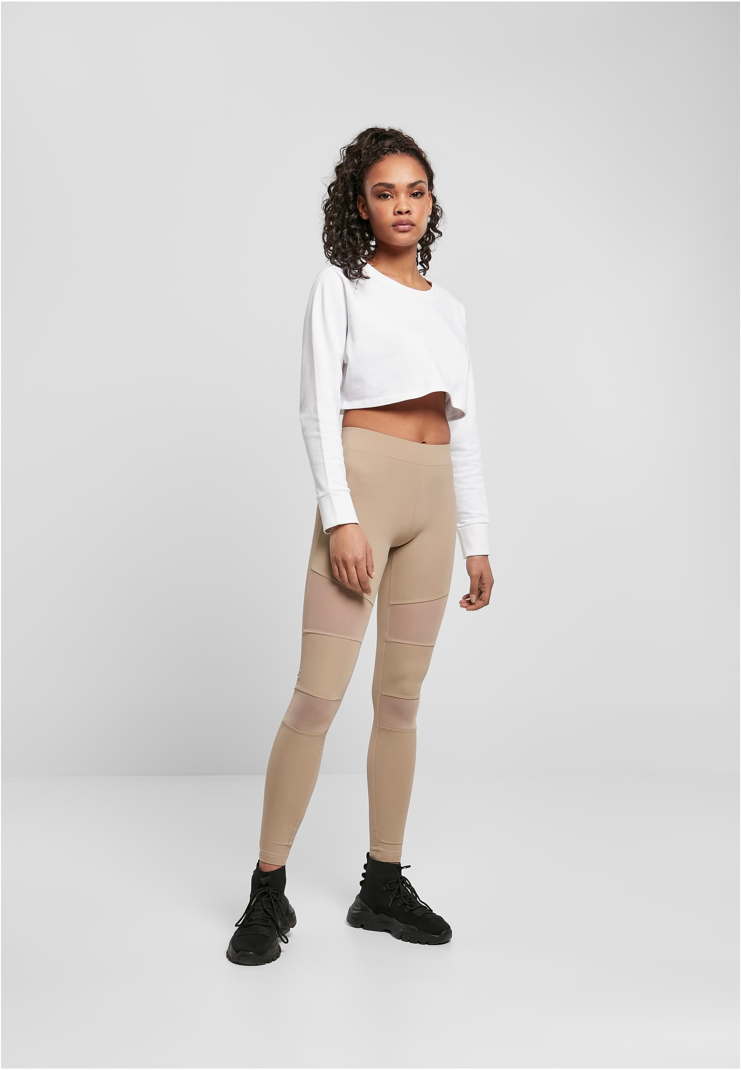 Helbild på en kvinna som bär varmgrå Ladies Tech Mesh Leggings med nätpaneler, kombinerat med en vit croppad tröja och svarta sneakers.