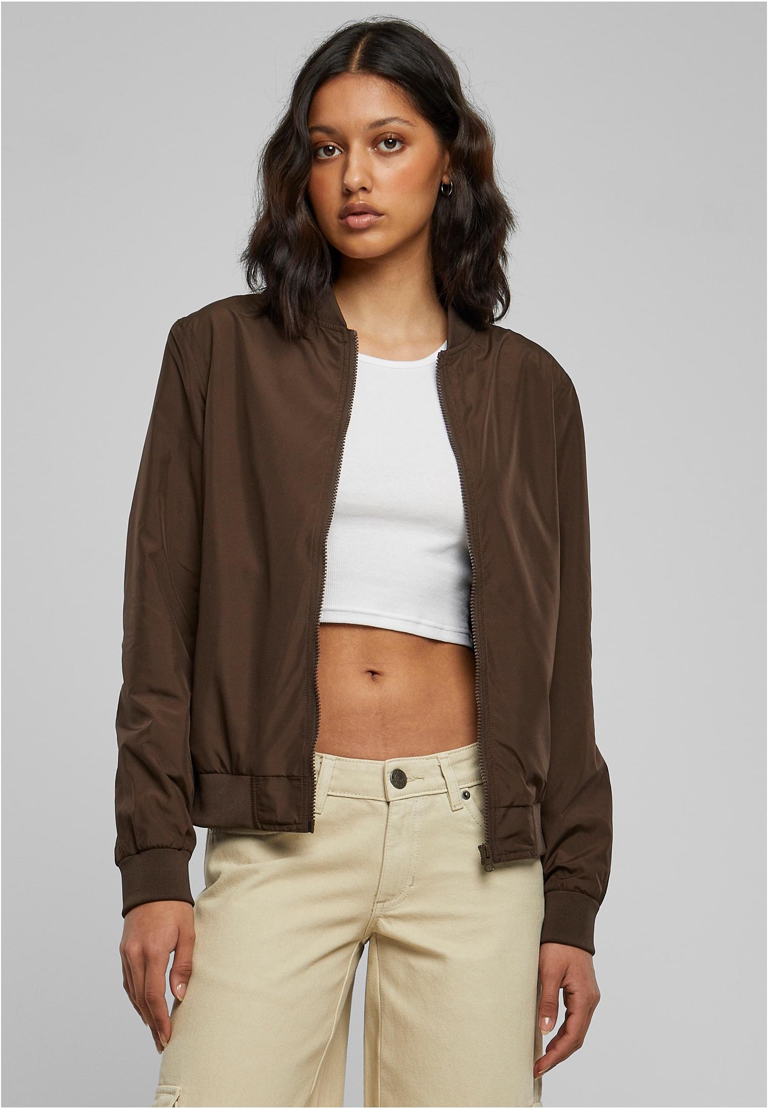 En kvinna bär en öppen brun UC Light Bomber Jacket med en vit crop top och beiga byxor.