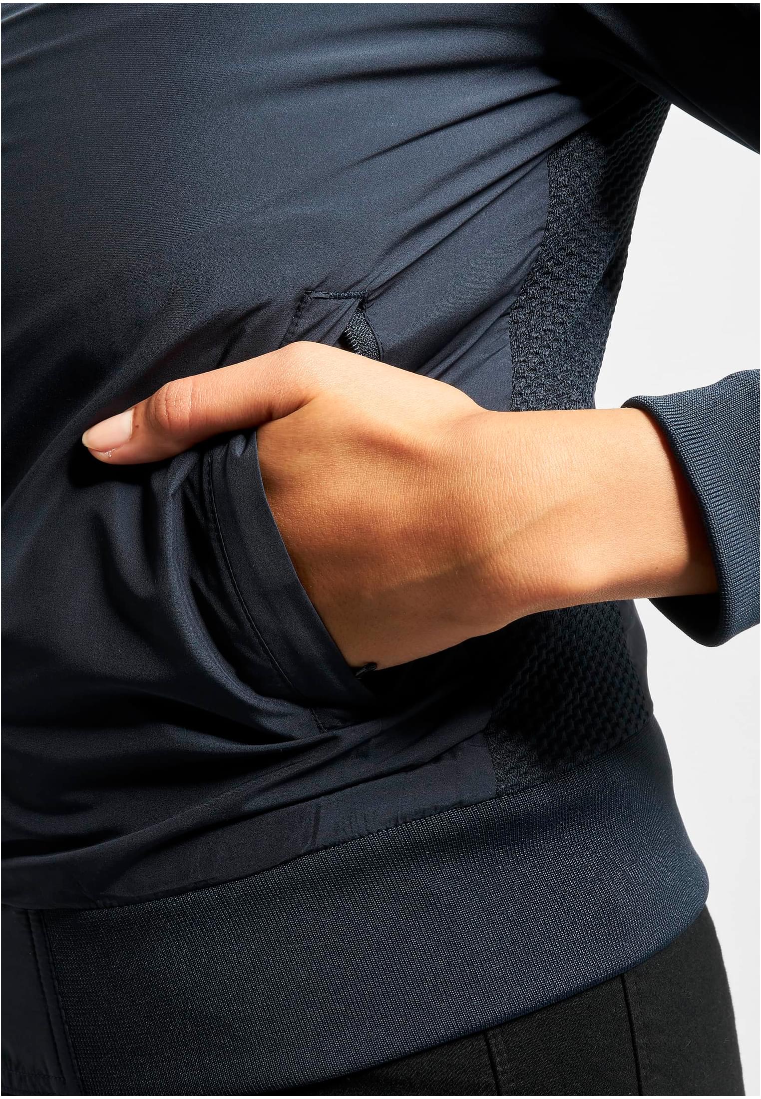 Närbild på en kvinna som sticker ner handen i fickan på en mörkblå UC Light Bomber Jacket.