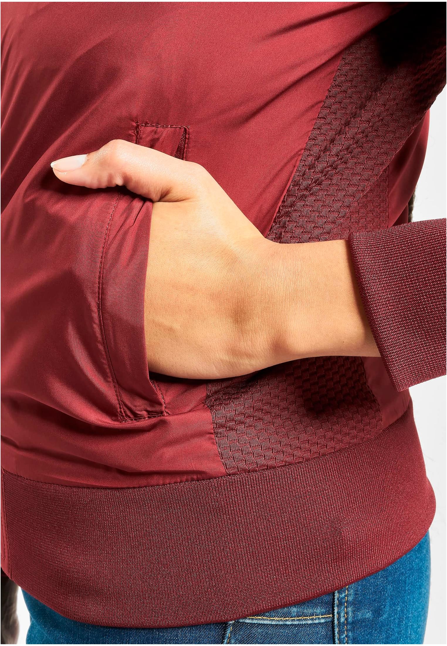 Närbild på fickan och den ribbade midjan på en vinröd bomberjacka.