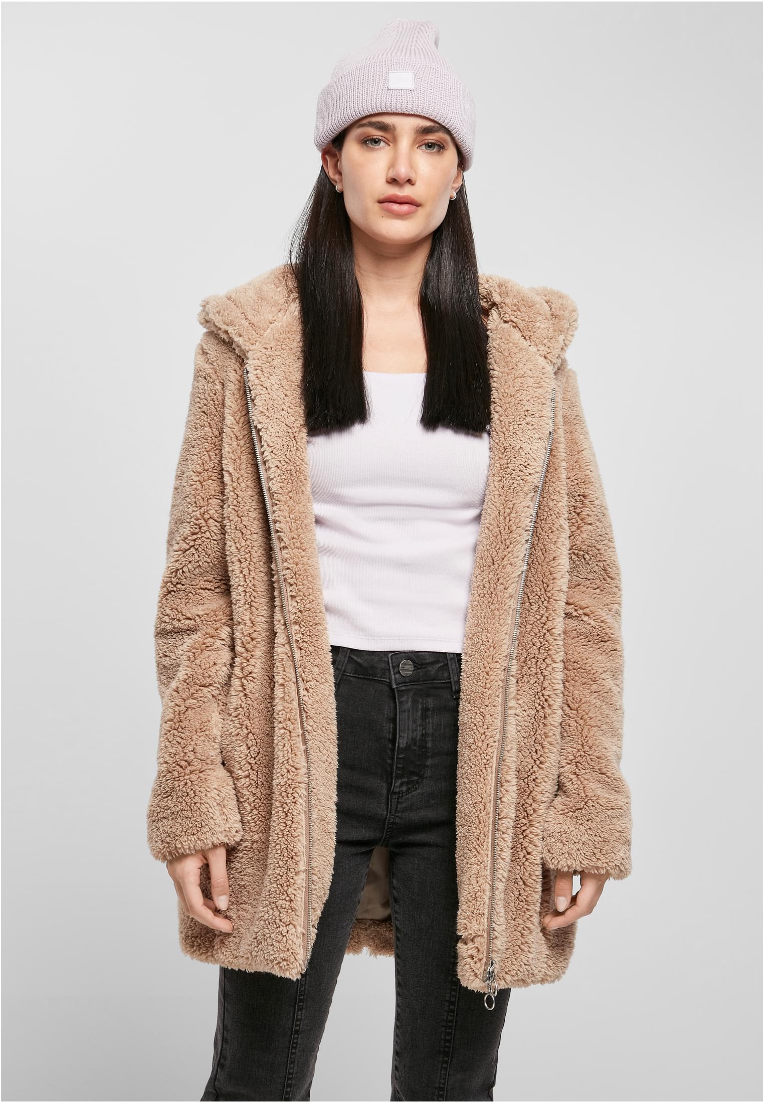 En kvinna bär en beige UC Sherpa Jacket öppen, med ett vitt linne, svarta jeans och en ljuslila mössa.