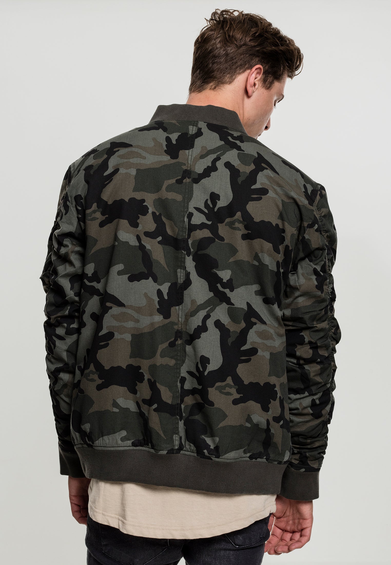 En man visar baksidan av en bomberjacka med grönt kamouflagemönster.