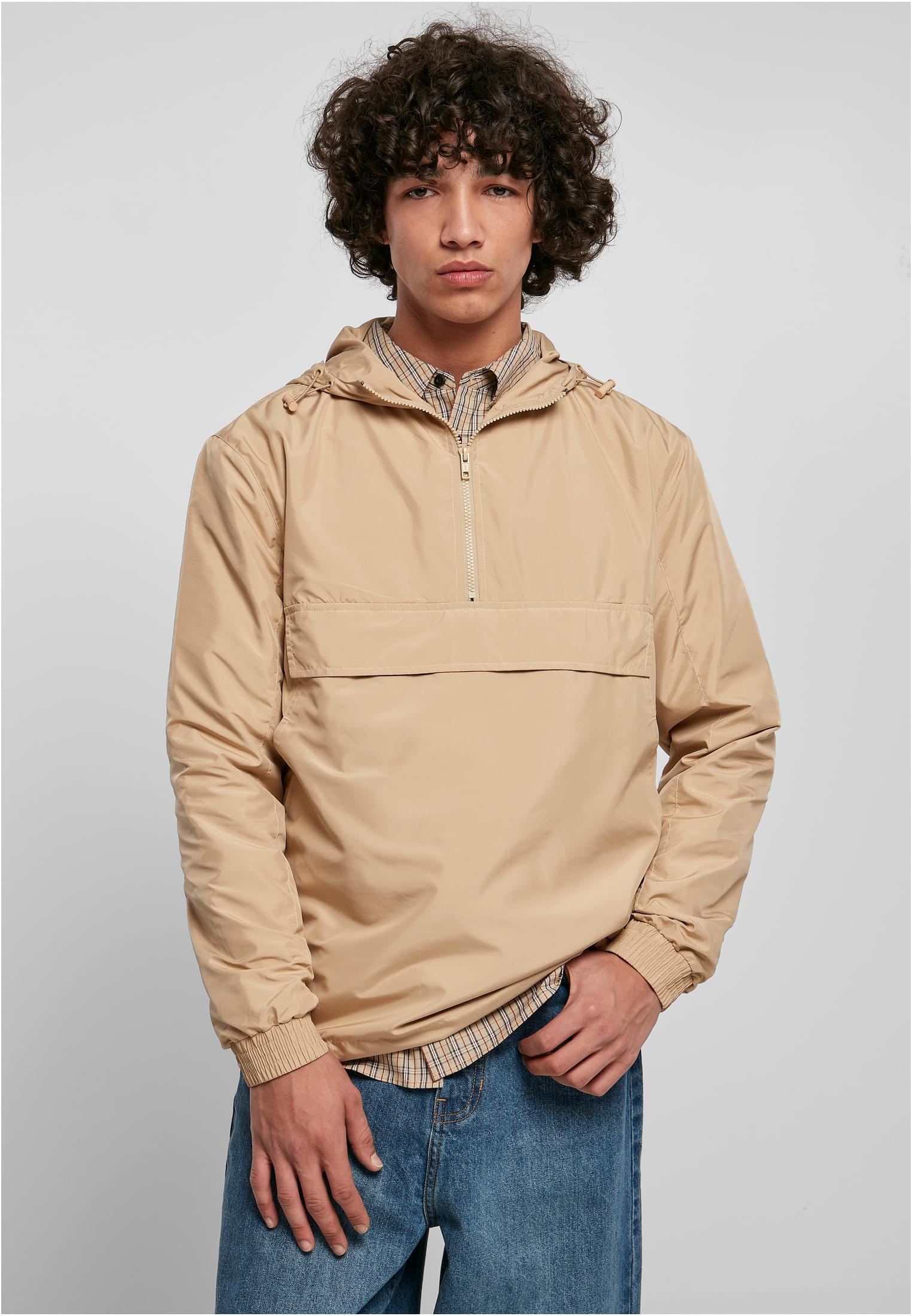 En manlig modell visar upp en beige UC Basic Pull Over Jacket, buren över en rutig skjorta och tillsammans med blå jeans.