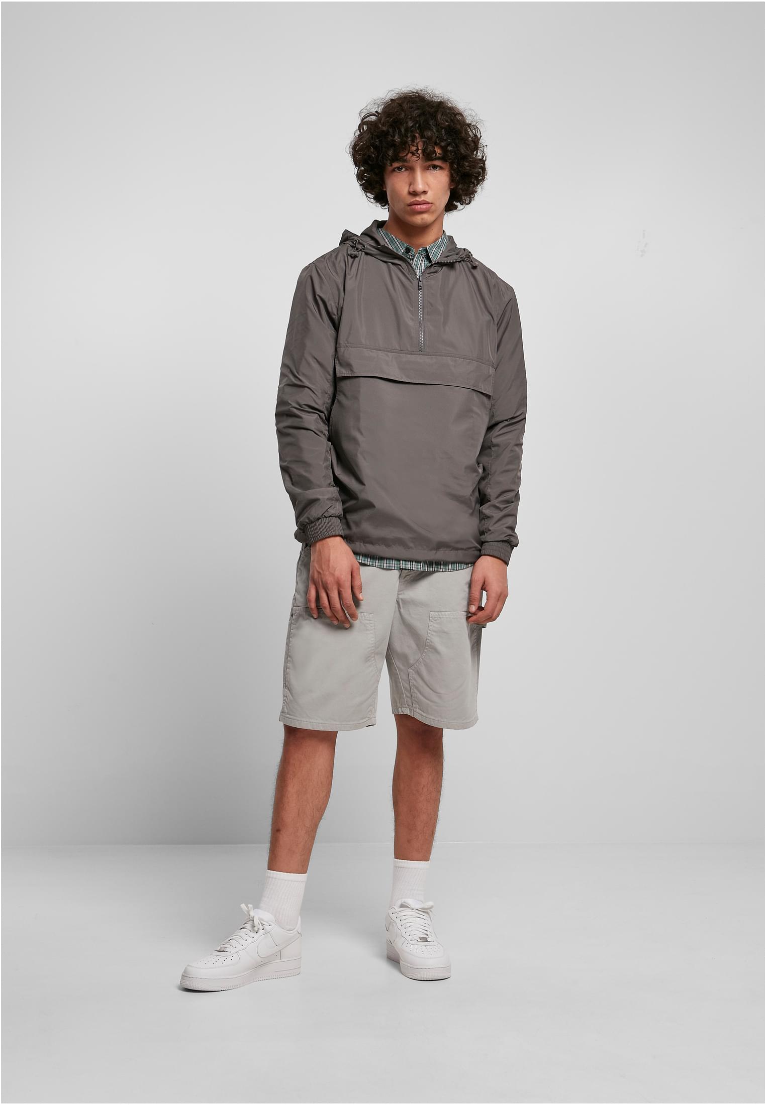 En manlig modell bär en mörkgrå UC Basic Pull Over Jacket med ljusgrå shorts och vita sneakers.